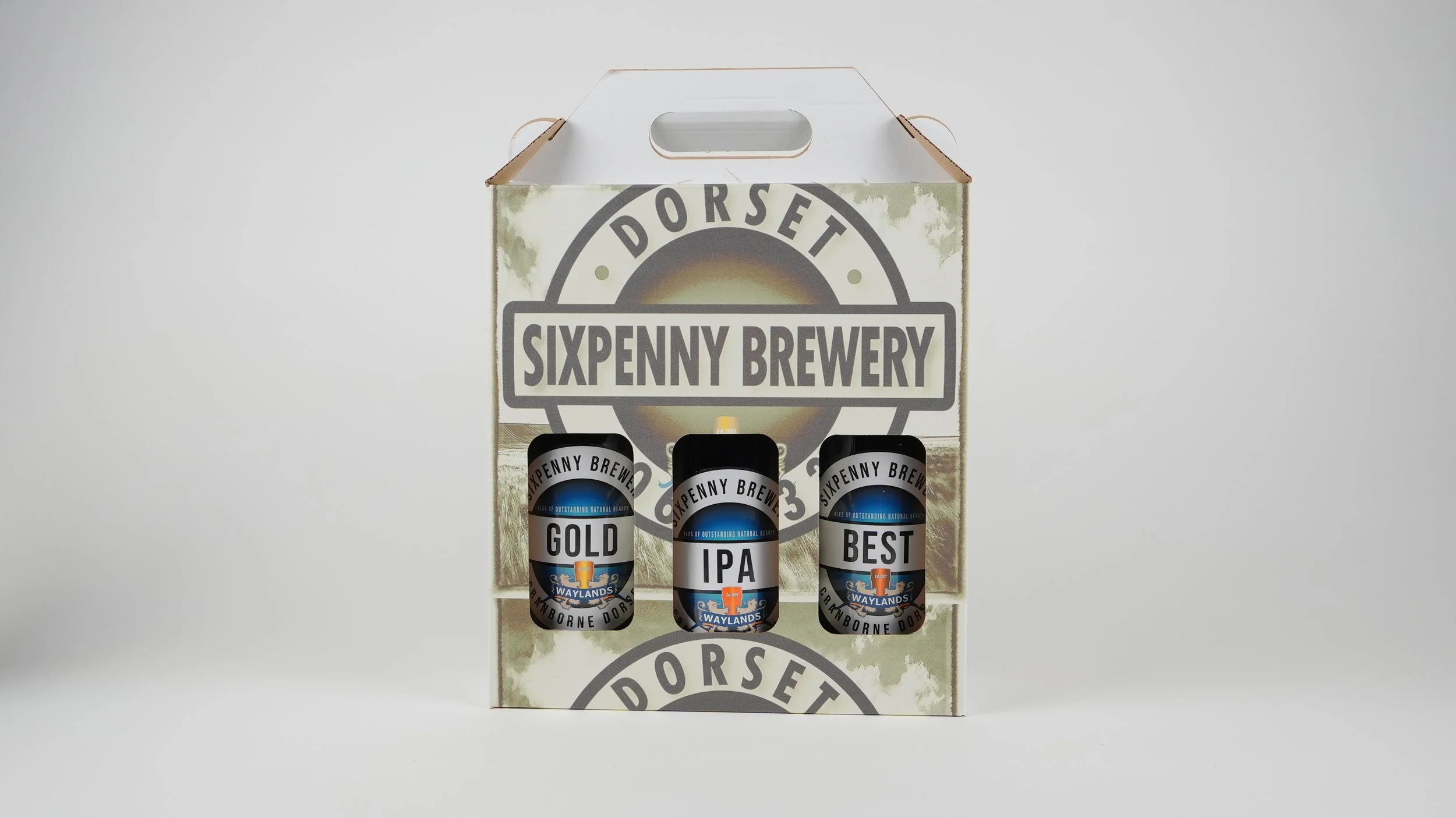 Sixpenny Brewery beer gift set with three cans labeled Gold, IPA, and Best, inside a cardboard carrier with Dorset branding on a plain white background.