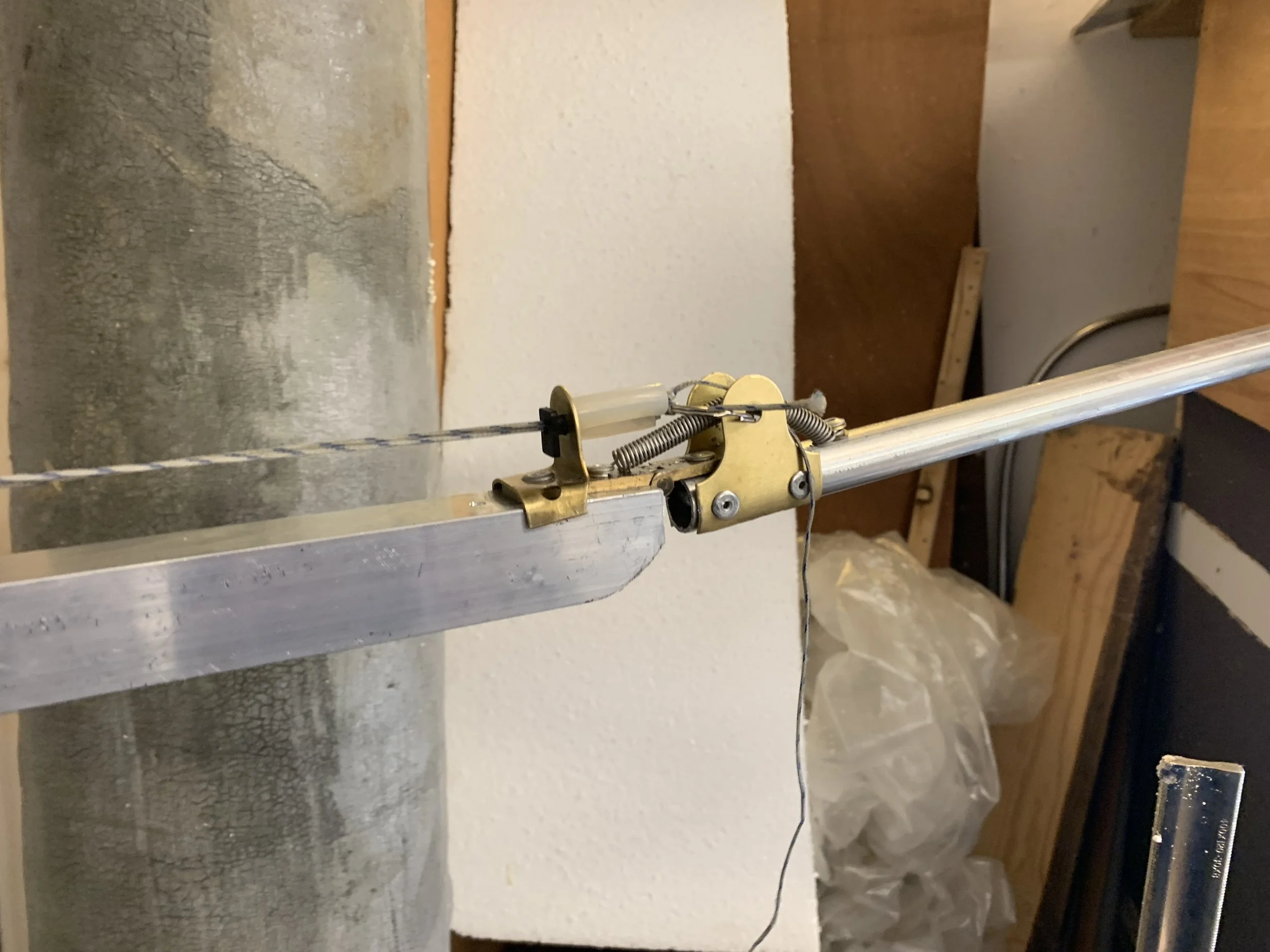 Close-up of a mechanical device with a metal rod, springs, and a pulley in a workshop setting.