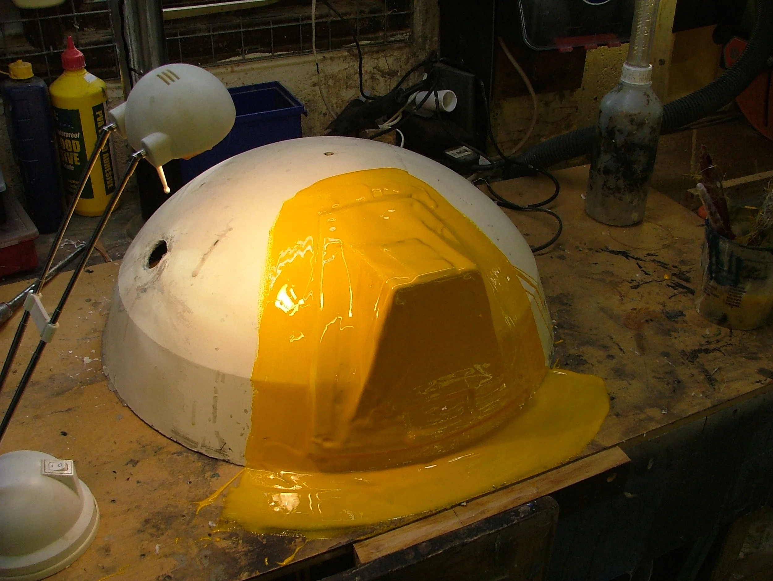 A white helmet shell with yellow resin being poured and spread inside.