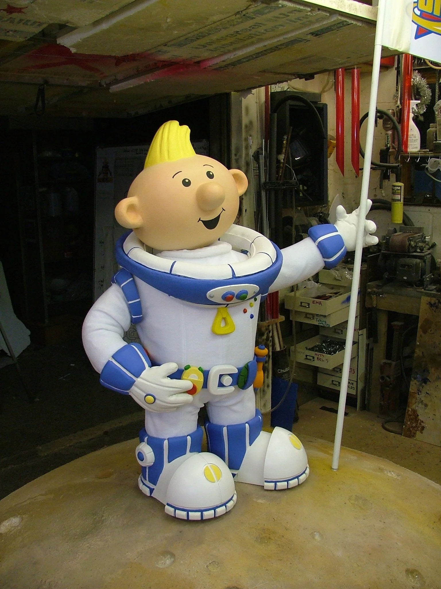 Photo of a large, colorful statue of a cartoon astronaut with a blonde hair, wearing a white and blue spacesuit, holding a flag.