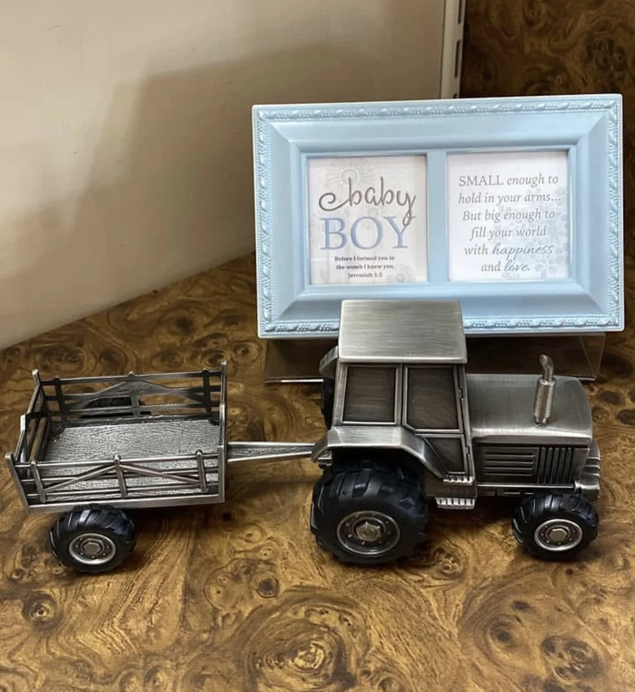 A baby bank metal toy tractor with a trailer sits on a wooden surface, with a blue framed sign in the background that has a baby boy poem.