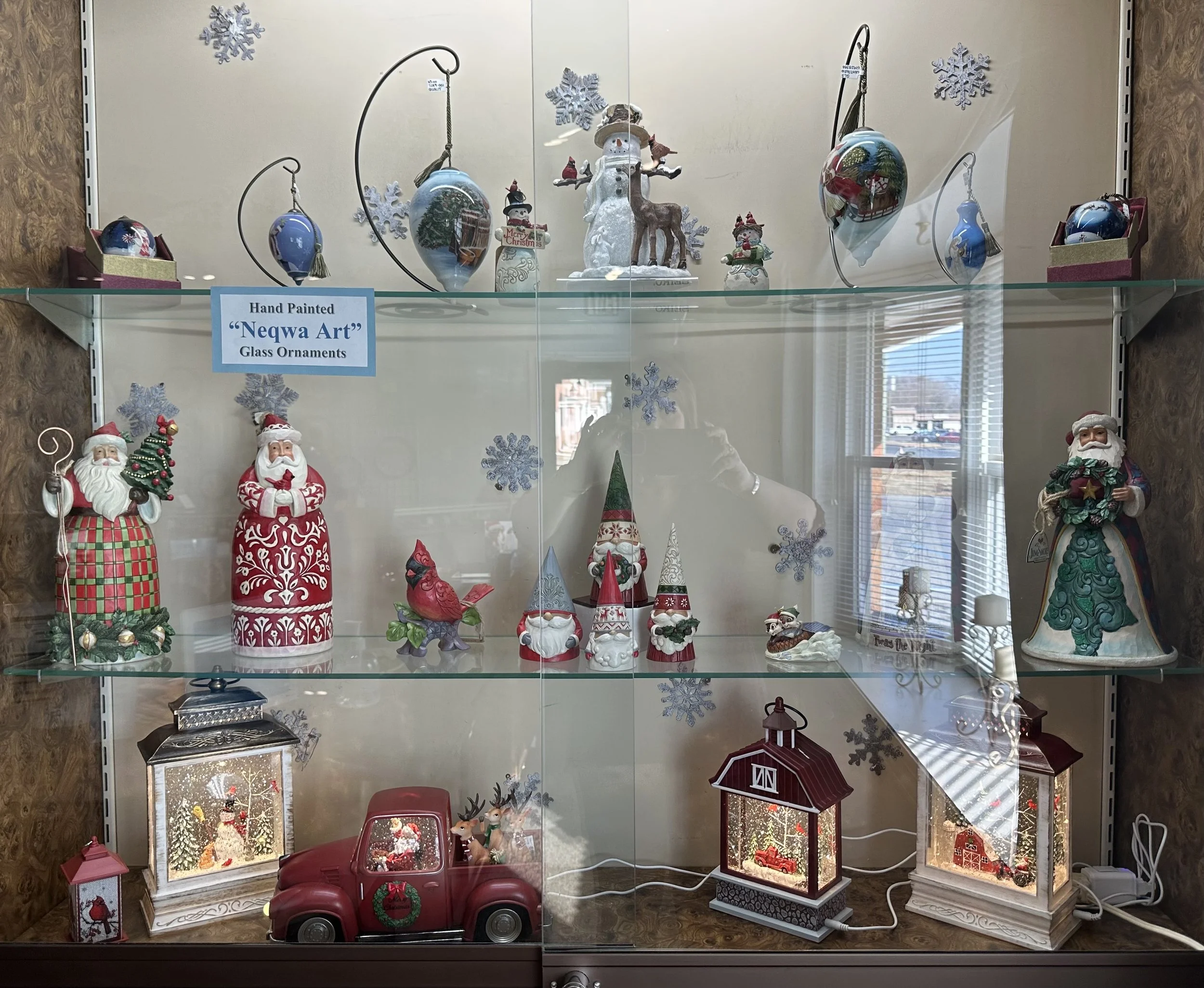 Display case with various Christmas decorations, including hand painted Ne Qua glass ornaments, Jim Shore Santa figurines, a snow globe motion lantern, a electric snow globe toy truck.