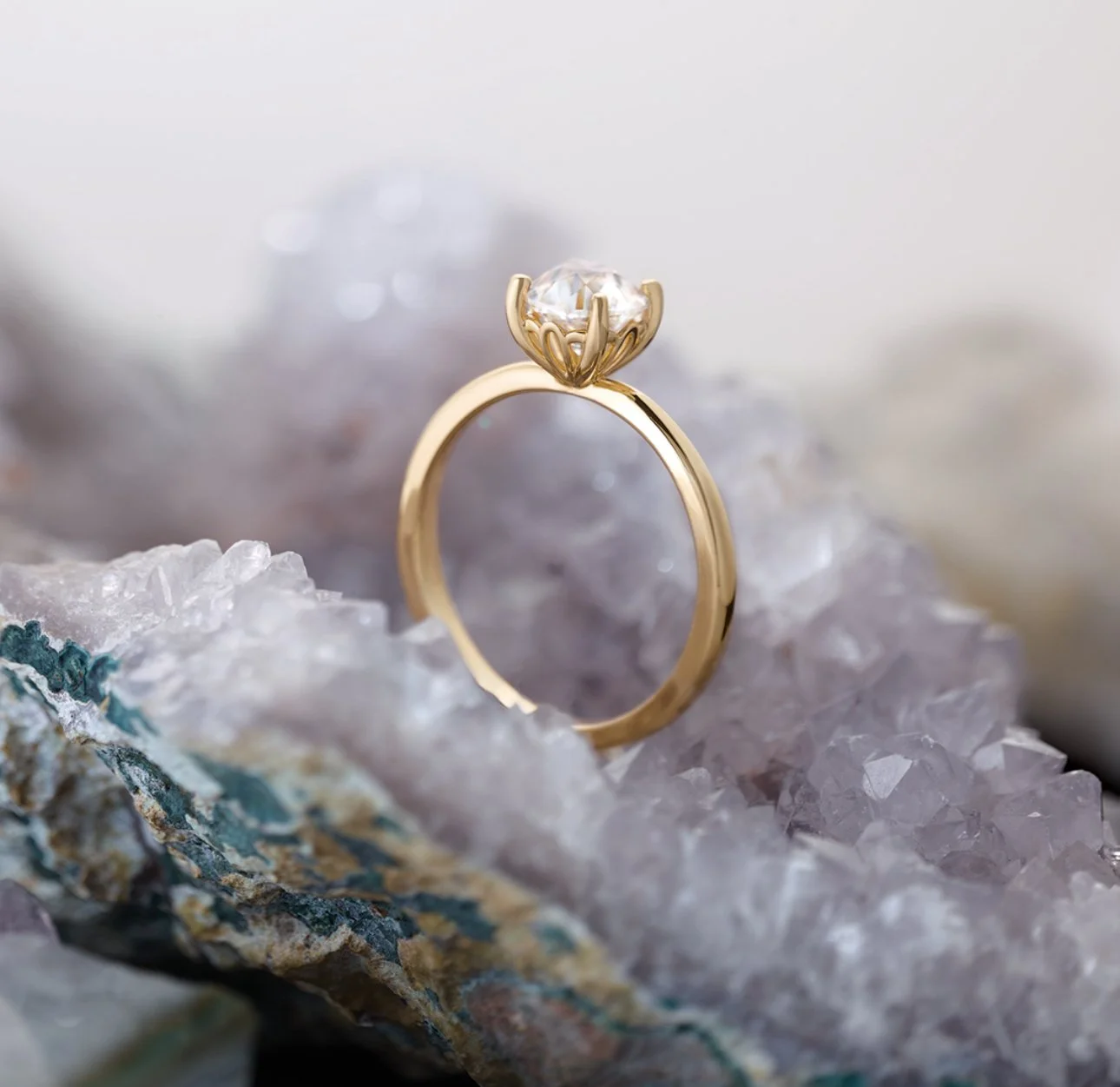A gold ring with a solitaire diamond setting on a rocky surface.