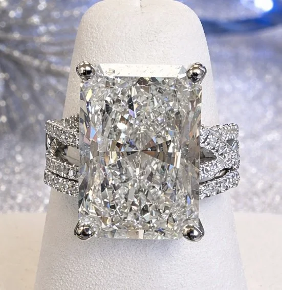 Close-up of a large, rectangular diamond engagement ring with a pavé band displayed on a white ring holder.