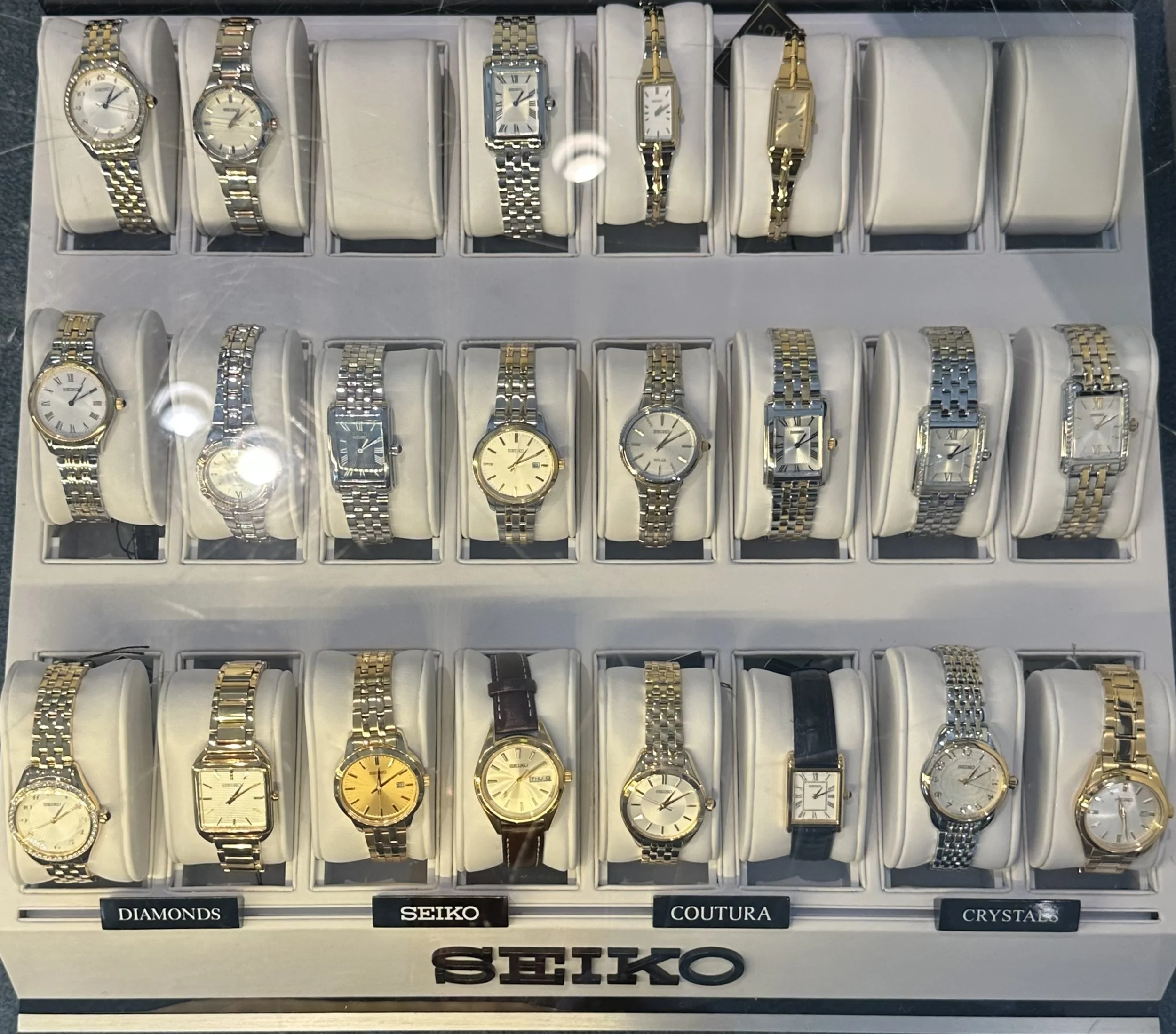 Display case with multiple rows of Seiko watches on white cushions, categorized as Diamonds, Seiko, Couture, and Crystals.