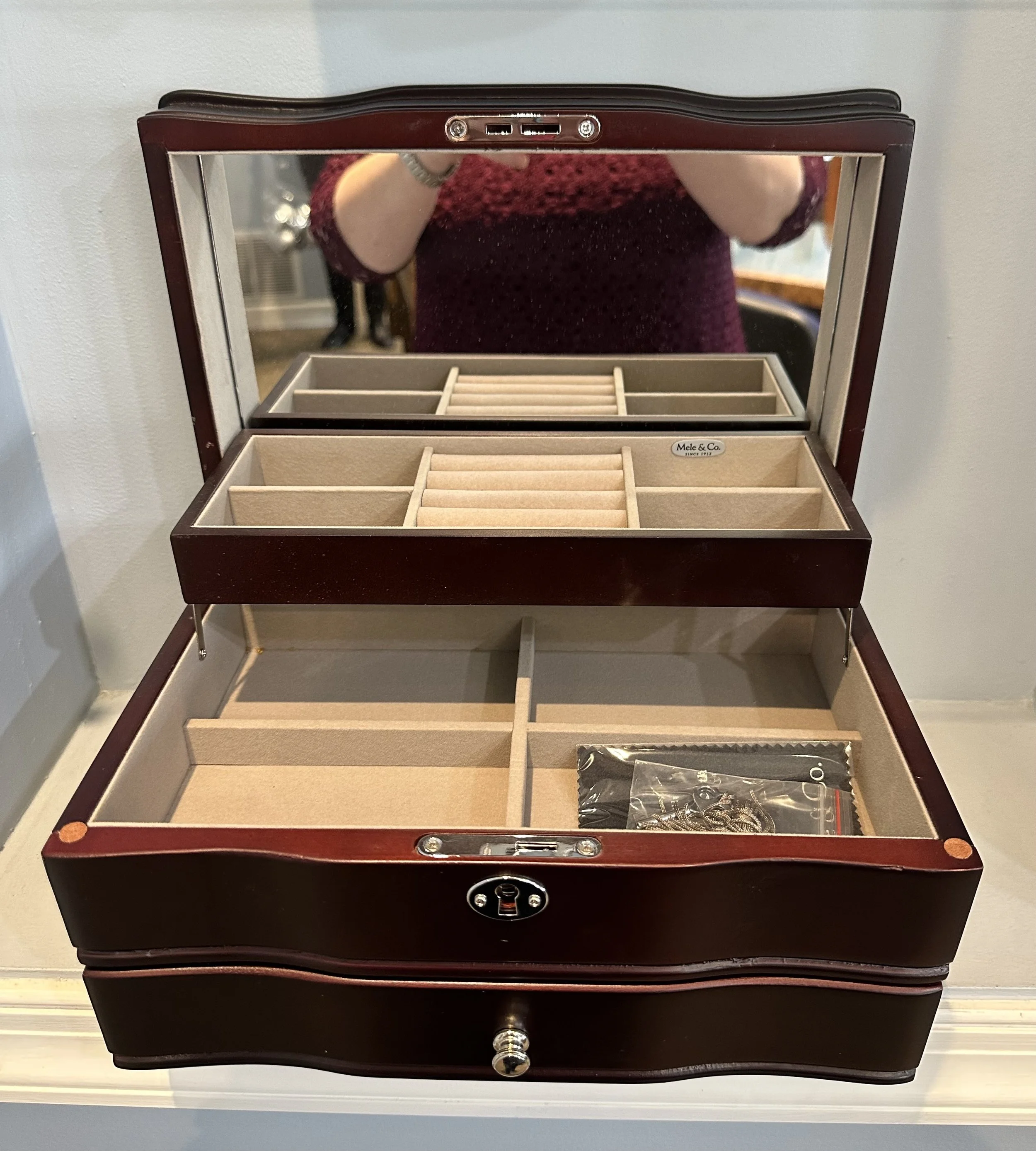 Open jewelry box with compartments and a mirror, with a person taking the photo reflected in the mirror.