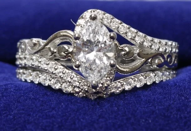 Close-up of a silver engagement ring with a large central diamond, surrounded by smaller diamonds, resting on a dark blue velvet background.