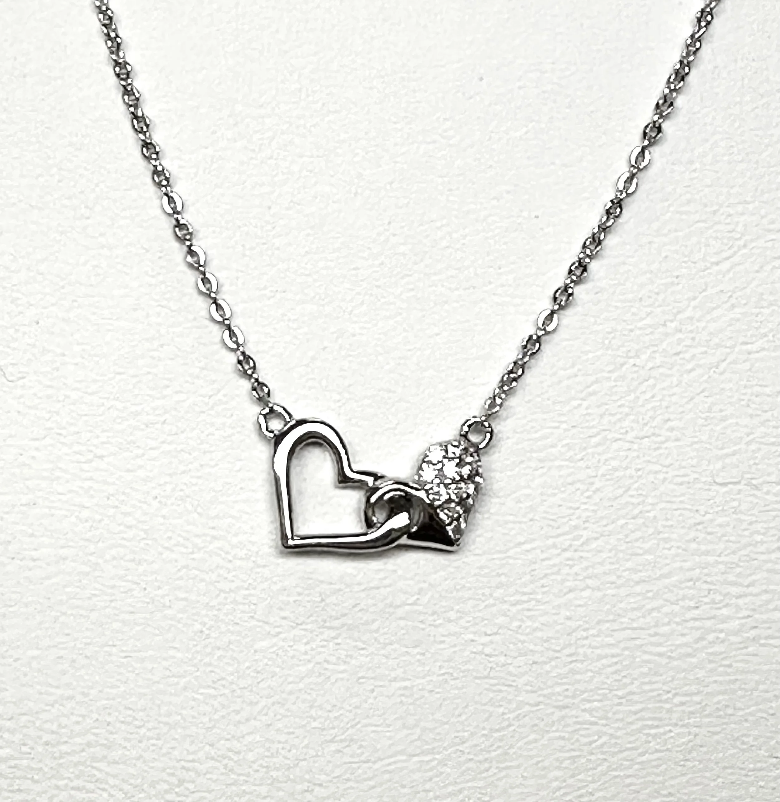 Silver necklace with a pendant of two intertwined hearts, one outlined and open, the other solid with small stones.