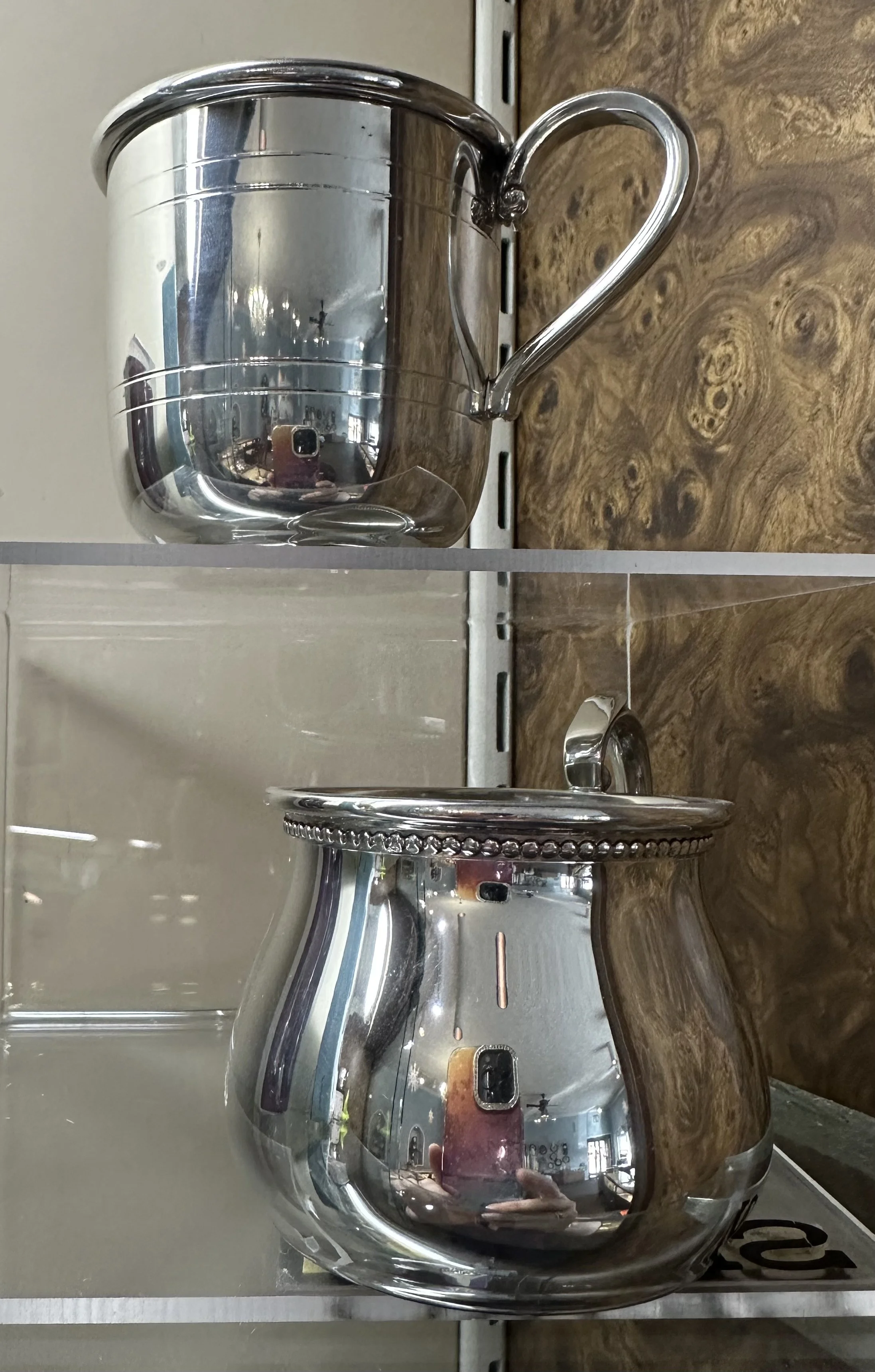 A round, pewter, reflective metal baby cup with a handle.