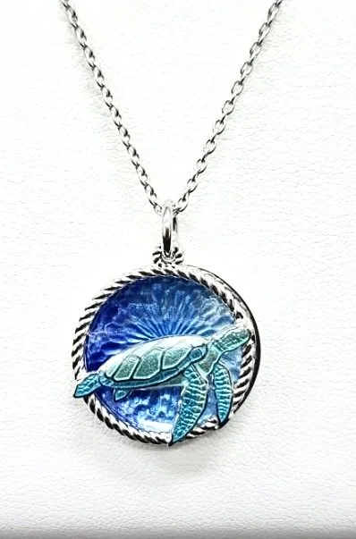 Silver necklace with a circular pendant featuring an engraved sea turtle against a blue enameled background.
