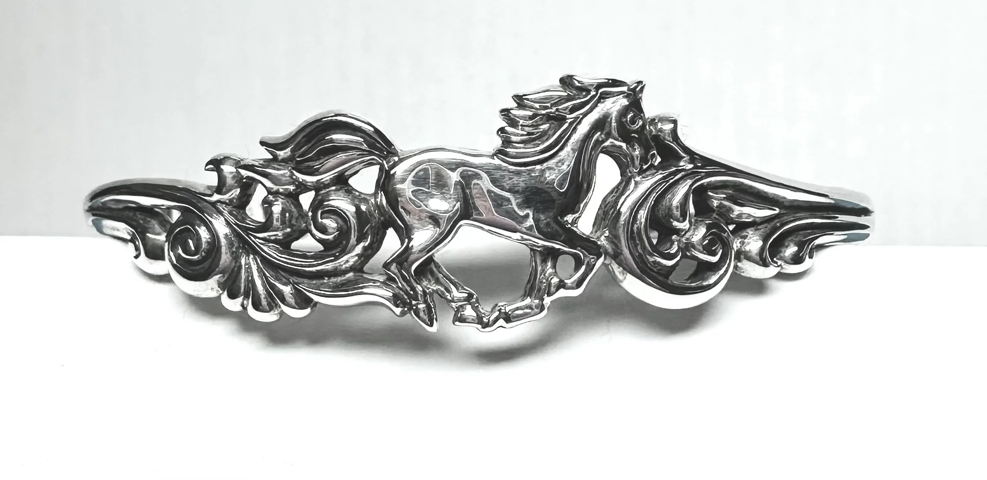 Silver cuff bracelet with a central horse figure and ornate, swirling designs on either side.