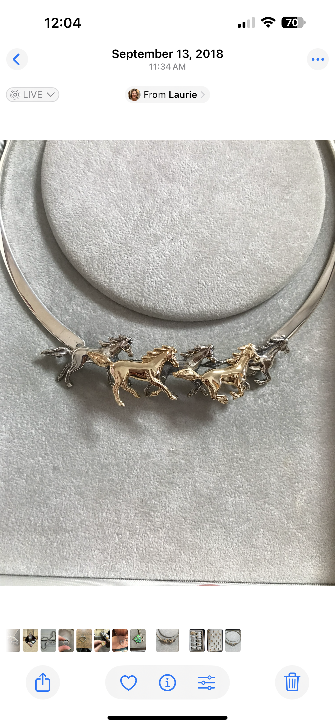 A jewelry display necklace with multiple gold and silver horse charms on a white, textured background.