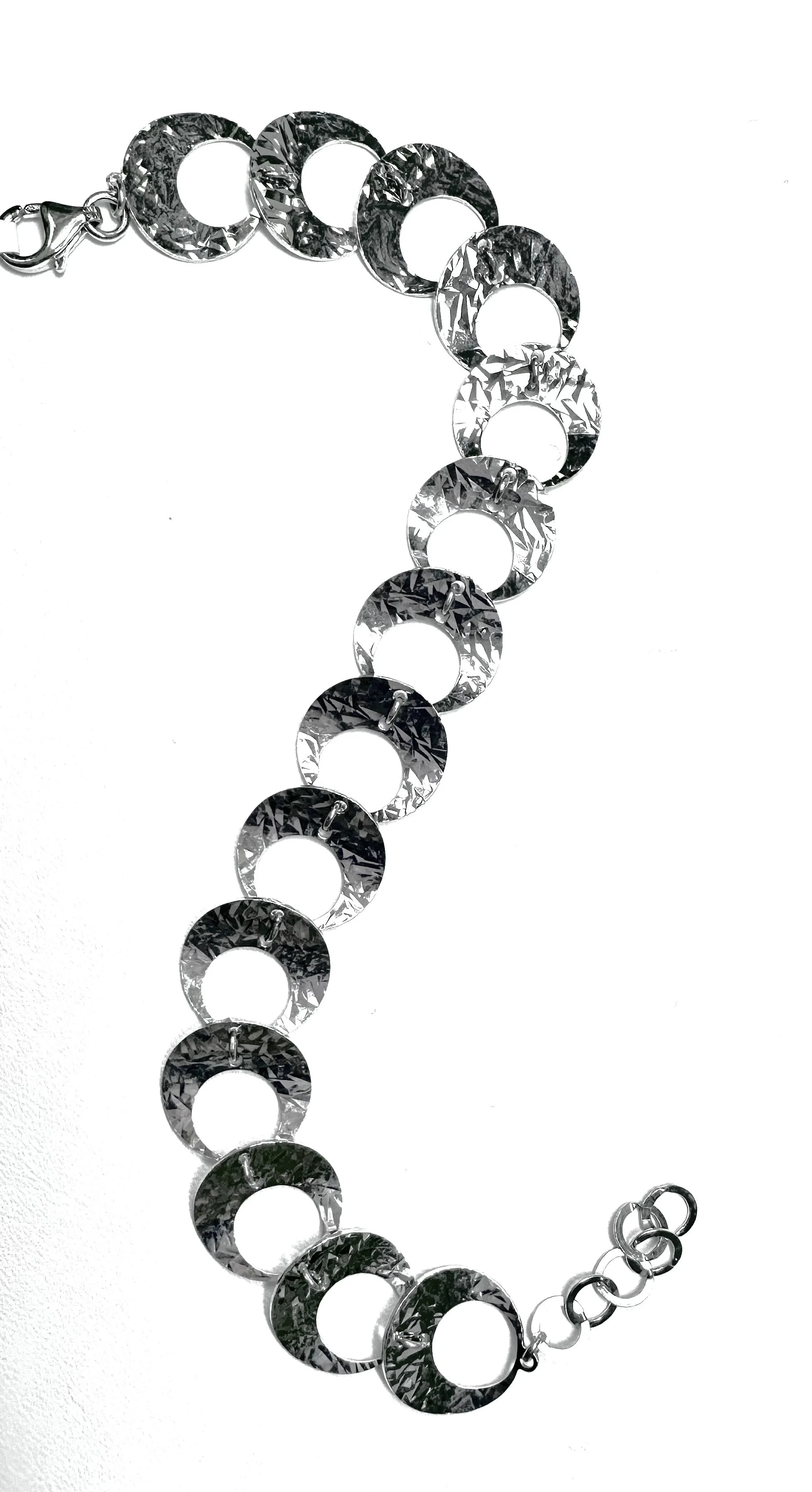 A silver bracelet with large, circular links, laid out on a white background.
