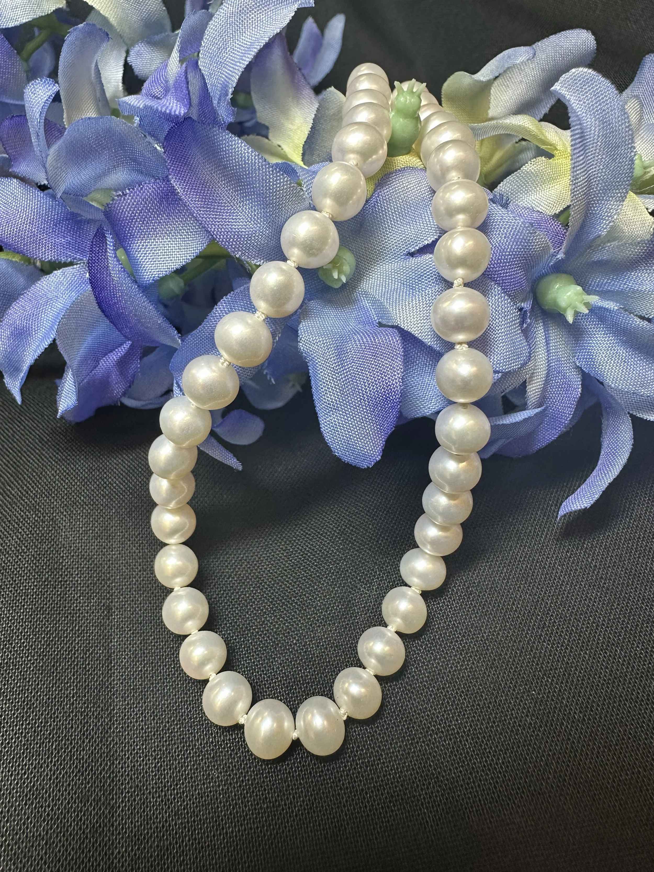 A string of white pearl necklace draped over purple and white fabric flowers on a black surface.