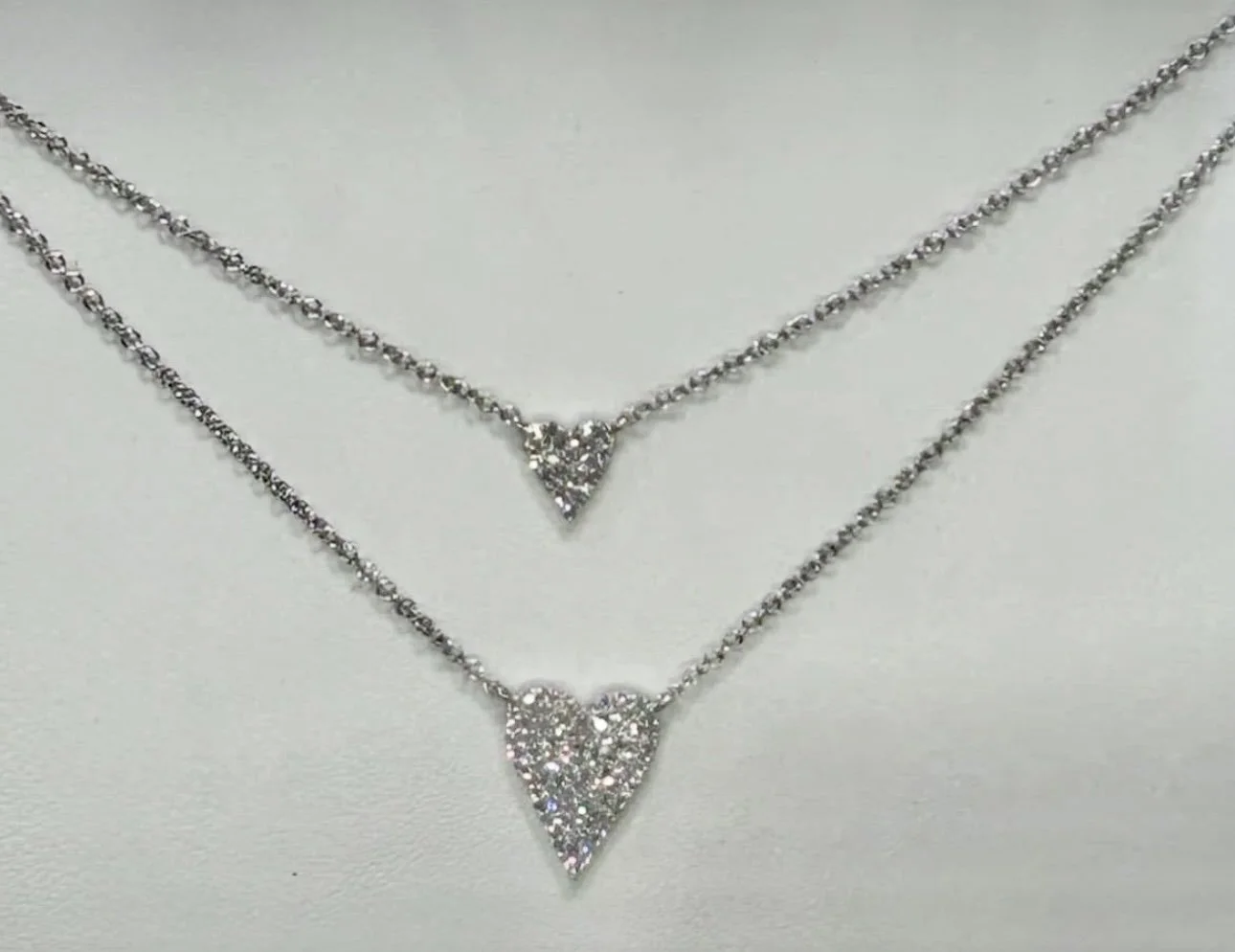 Two silver necklaces with triangle-shaped pendants encrusted with small clear stones, displayed on a white surface.