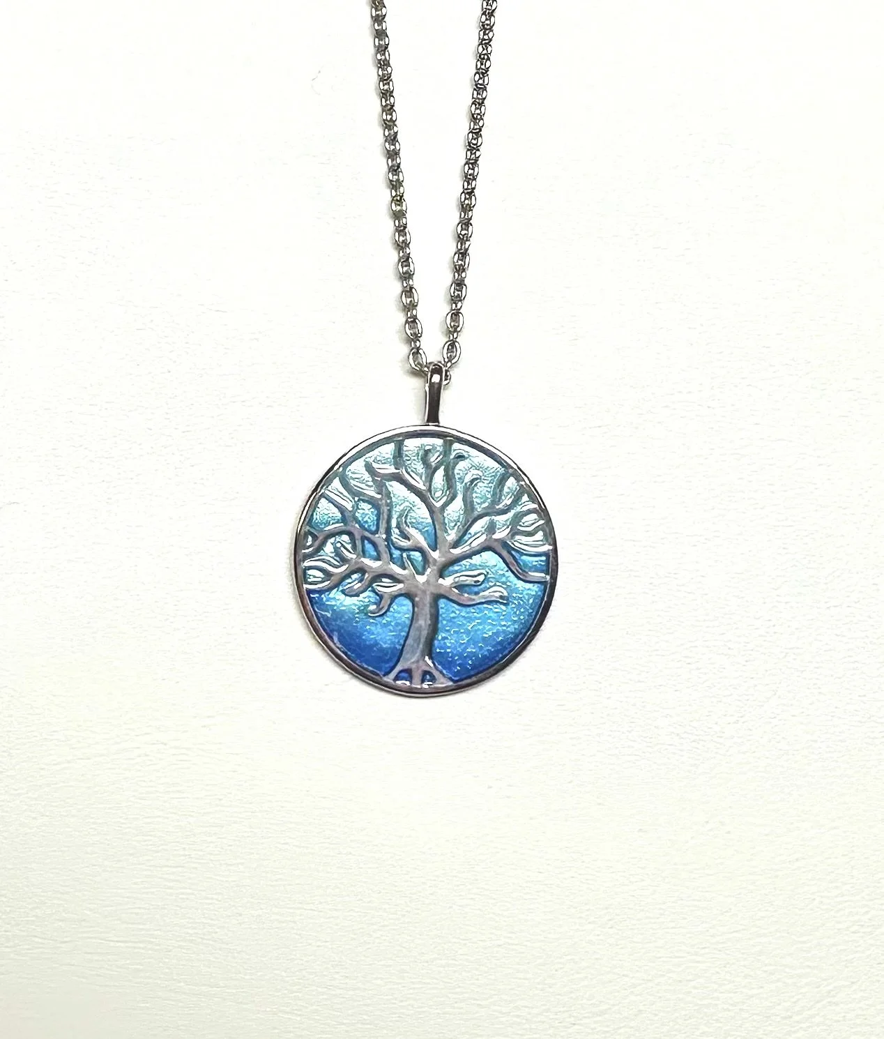 Silver necklace with a round pendant featuring a tree design and blue background.