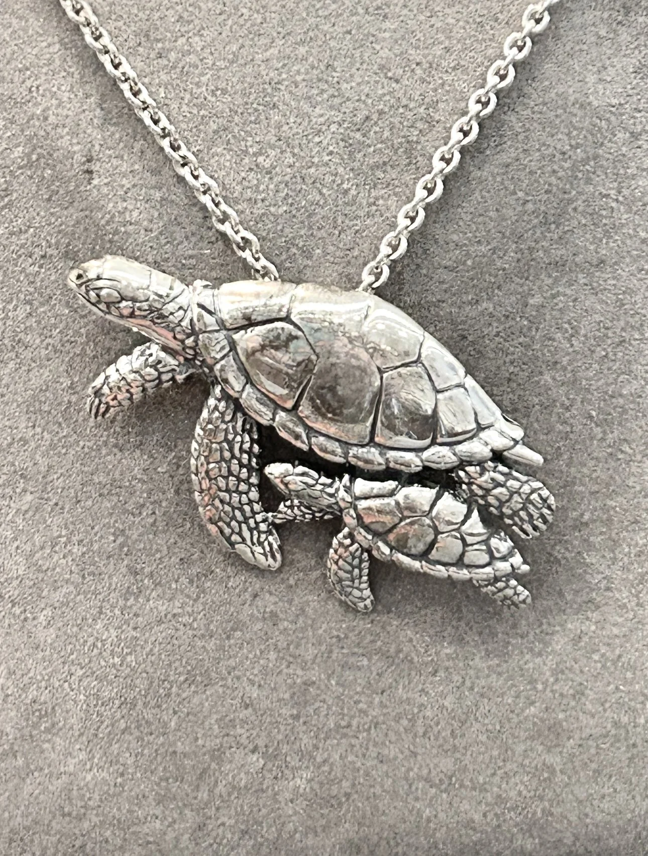 A silver turtle-shaped pendant necklace on a dark gray background.