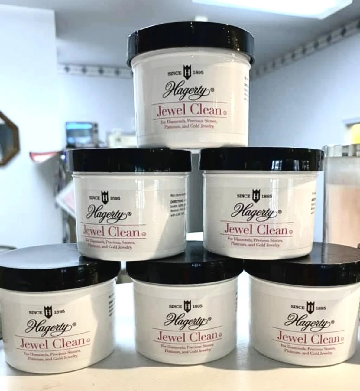 Six containers of Hagerty Jewel Clean jewelry cleaner arranged on a three-tiered display shelf.