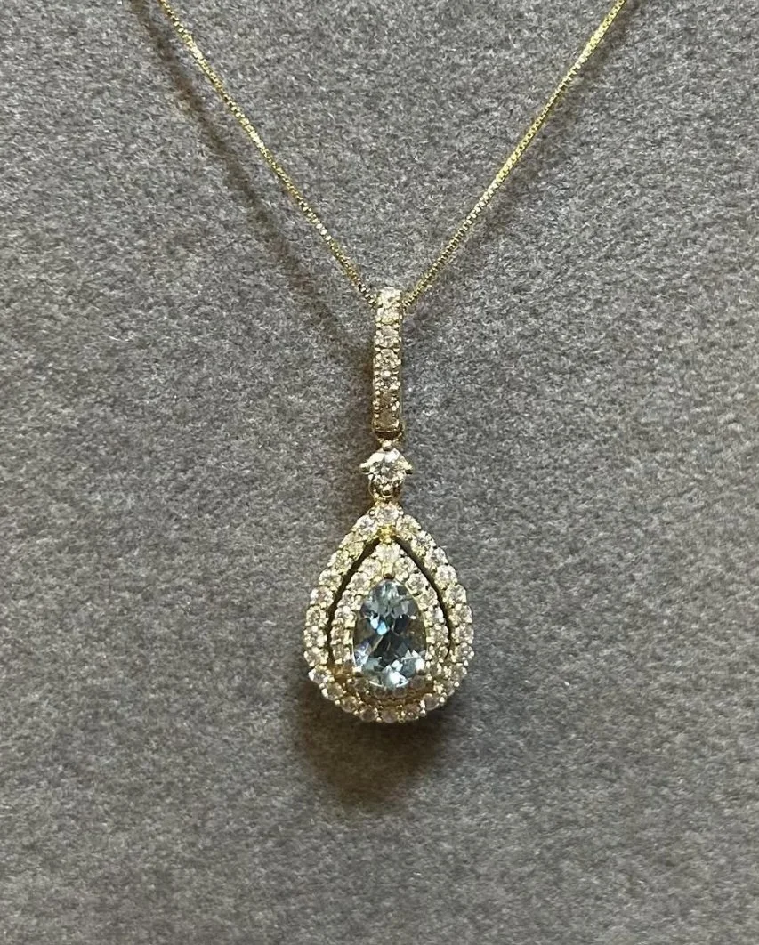 Gold necklace with a teardrop-shaped clear gemstone pendant surrounded by small diamonds.