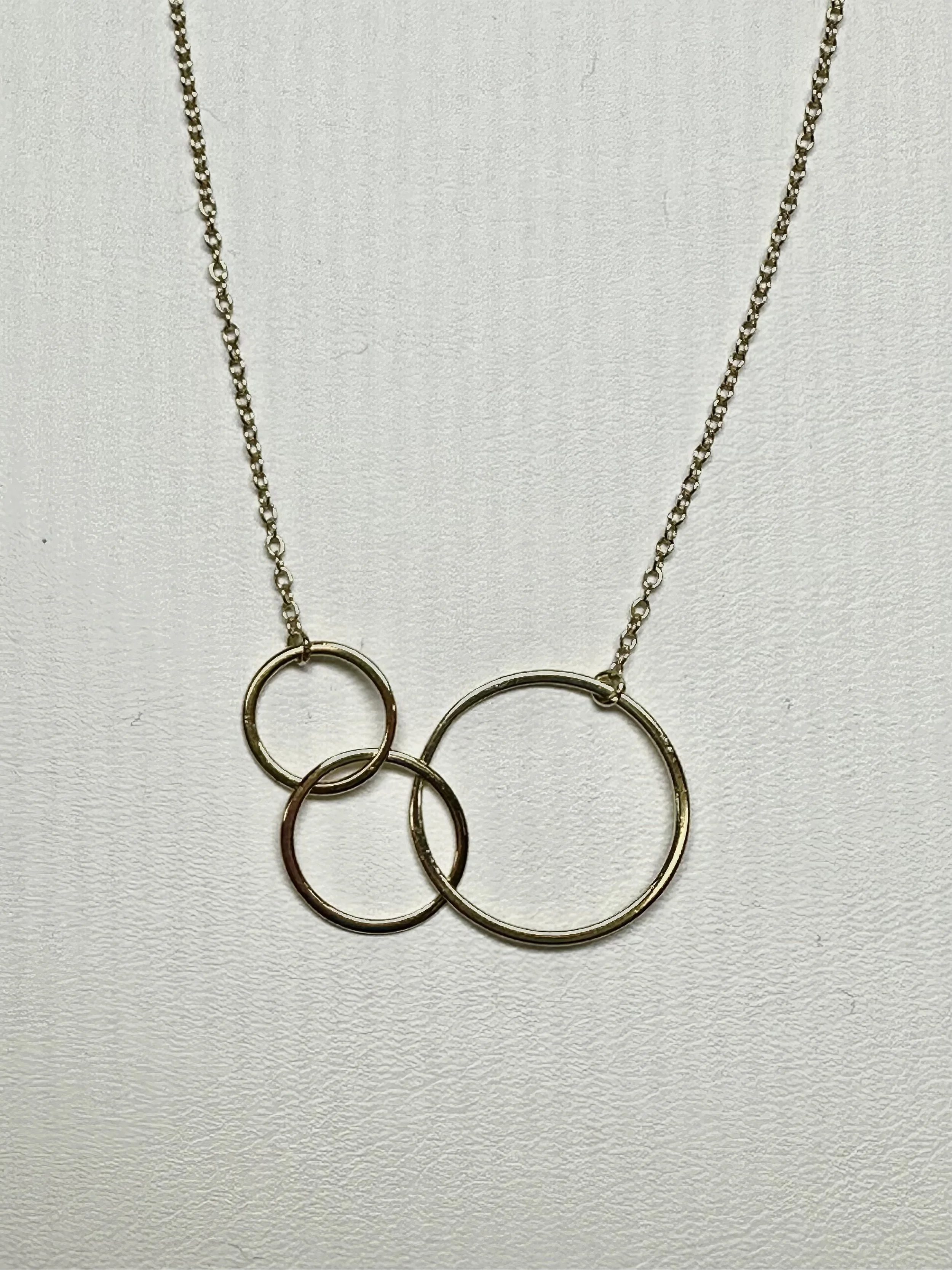 A gold plated silver necklace with a pendant of four interlinked circles of different sizes, hanging against a plain white background.