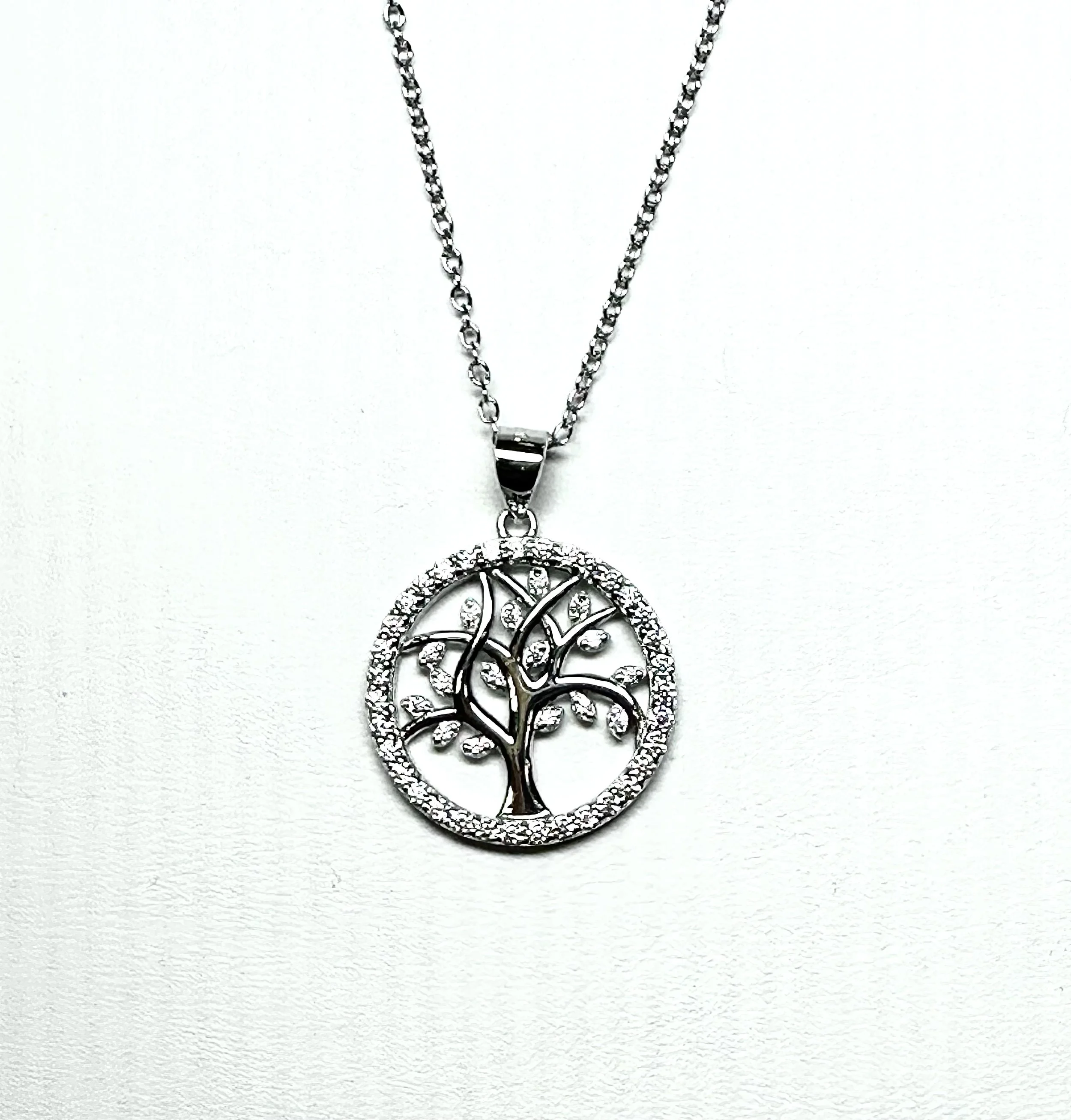 Silver necklace with a round pendant featuring a tree design with crystal accents.
