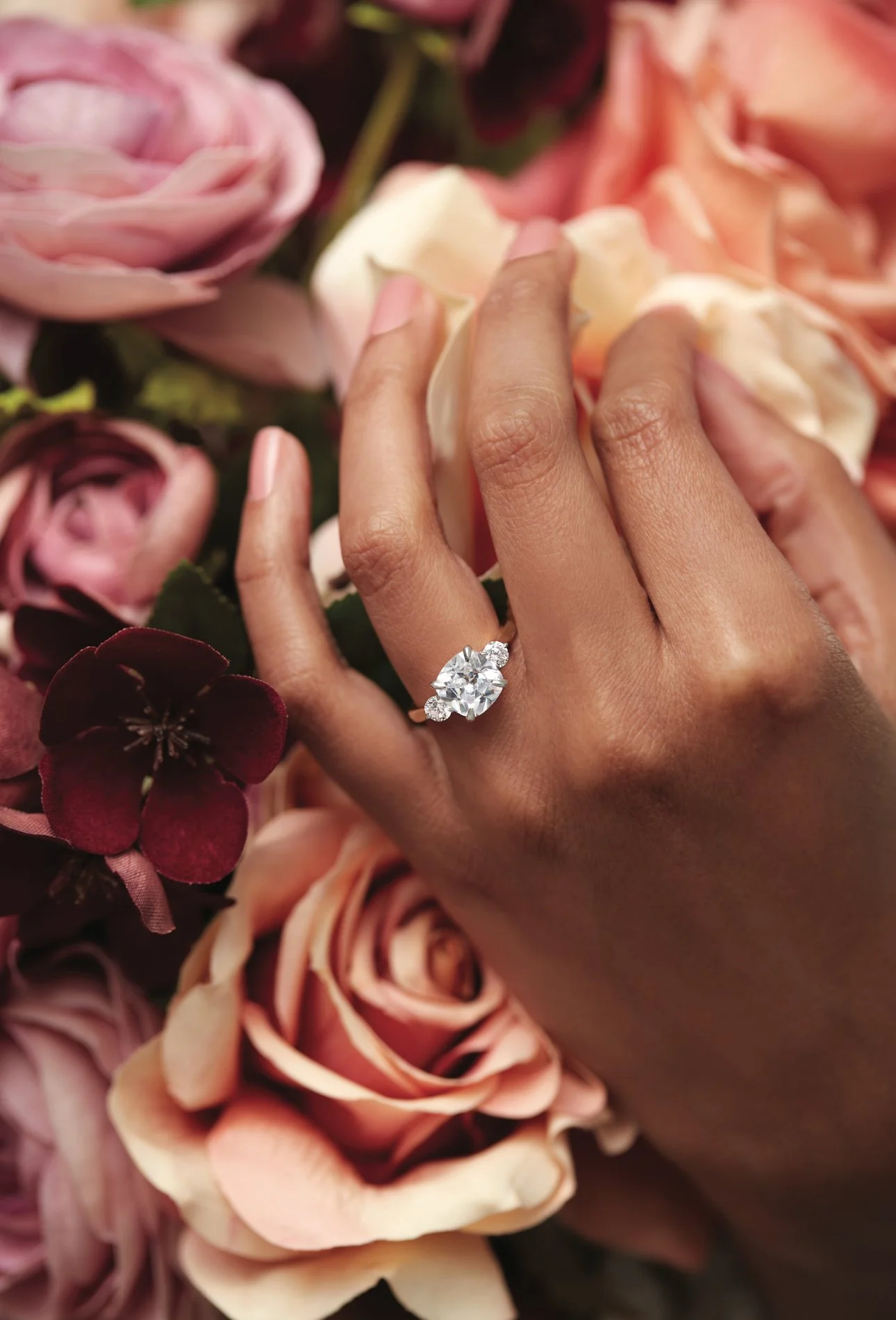 Close-up of a hand with an engagement ring, surrounded by pink and purple roses.