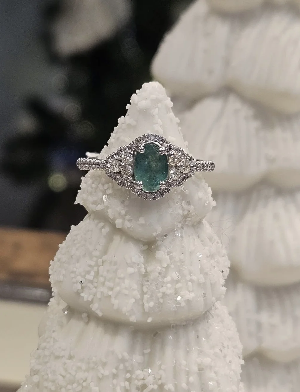 A silver ring with an oval turquoise gemstone surrounded by small clear stones, displayed on a white textured cone-shaped object.