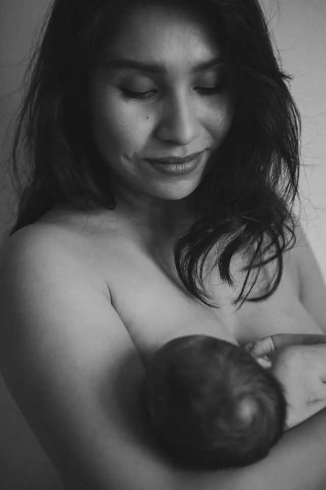 A woman is breastfeeding her newborn baby, whilst receiving breastfeeding support, in Maidenhead, from her birth and postnatal doula, Cara Jordan. The woman has long dark hair.