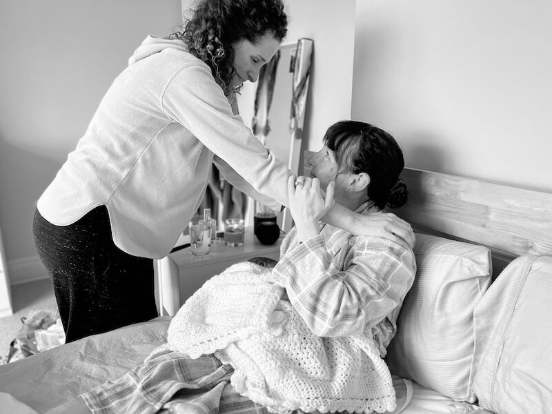 A woman who has just birthed, sits in bed cuddling her baby, Cara, a doula & night Nanny in West London, Maidenhead & Reading greats her warmly, they are in Reading.