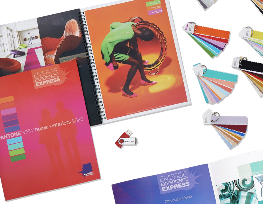Color swatch sample books, a Pantone color guide, and an open magazine featuring interior design and fashion photos on a white table.