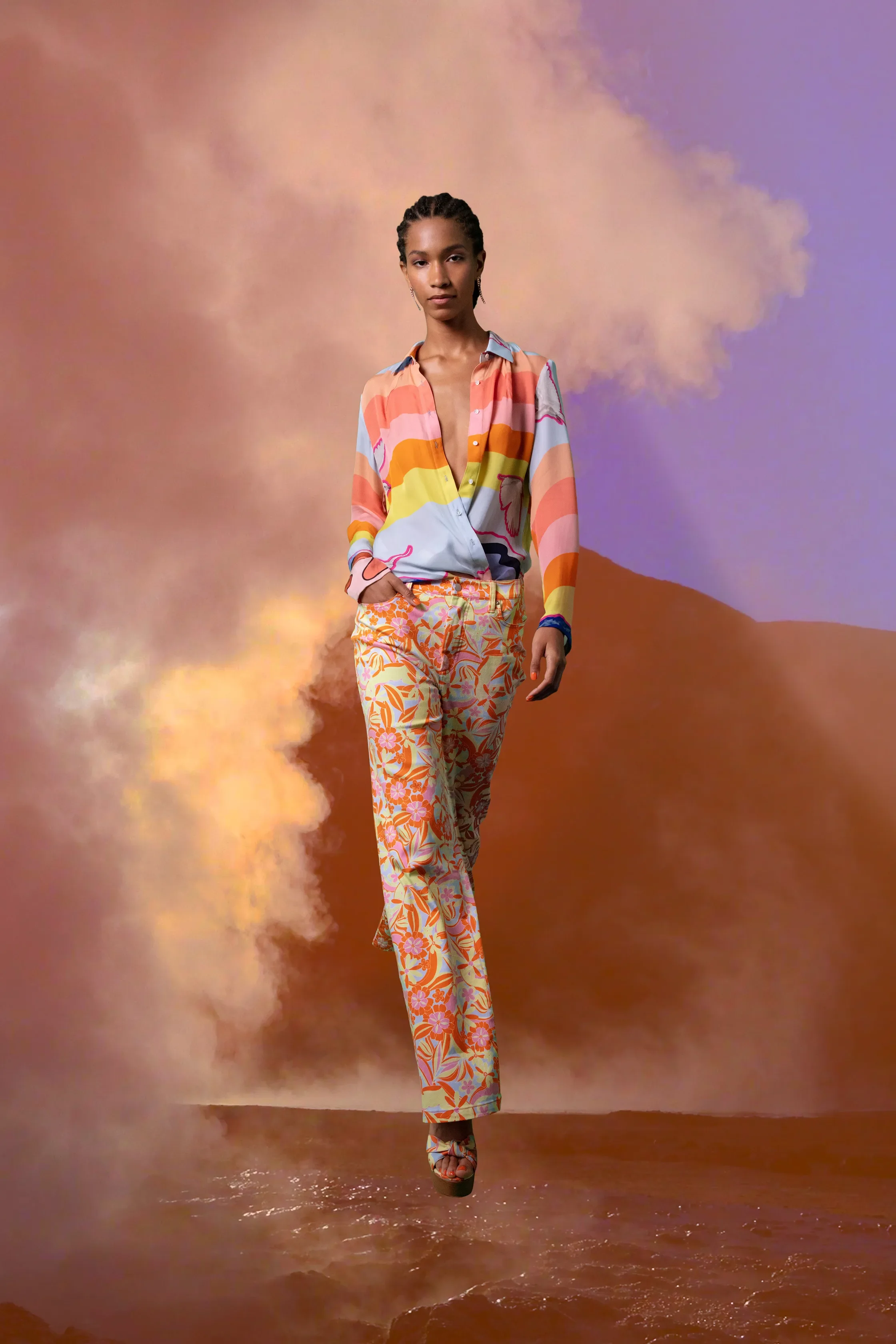 Woman in colorful patterned clothing walking through a desert landscape with dust and a cloudy sky.