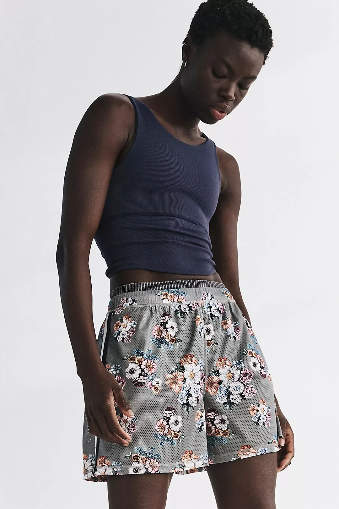 A woman wearing a dark navy sleeveless tank top and gray floral-patterned shorts against a plain white background.