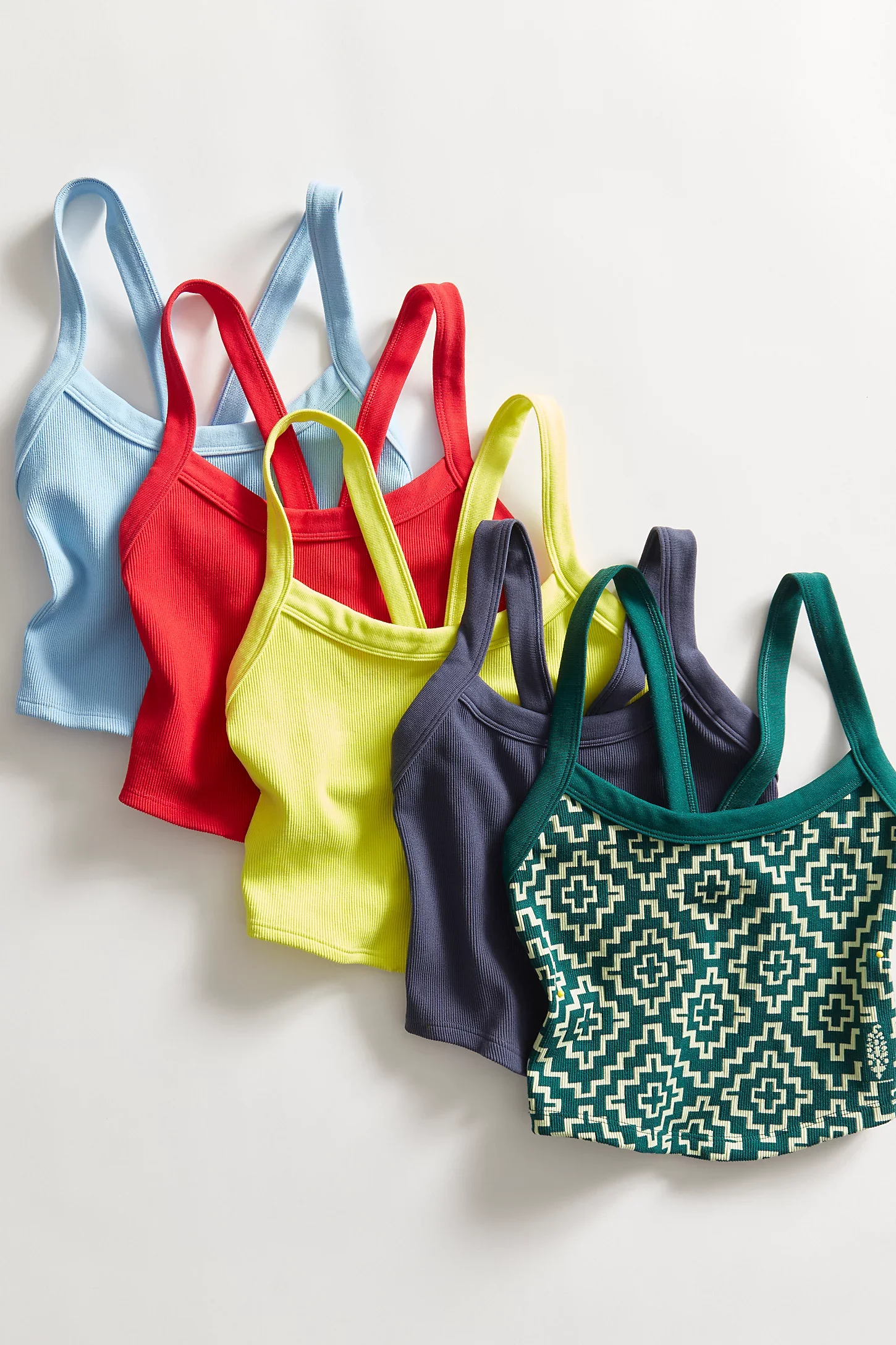 Collection of colorful tank tops in blue, red, yellow, dark gray, and patterned green and white, laid out on a white surface.