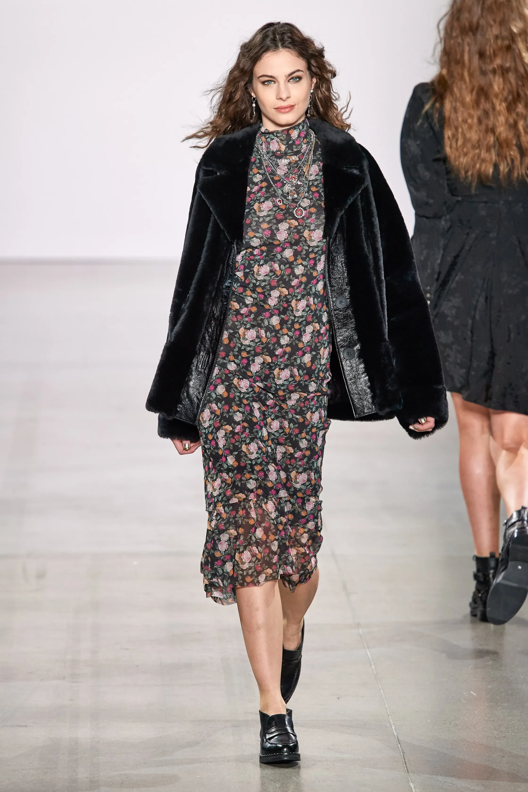 Model walking on runway wearing a floral dress with a black fur coat and black shoes.