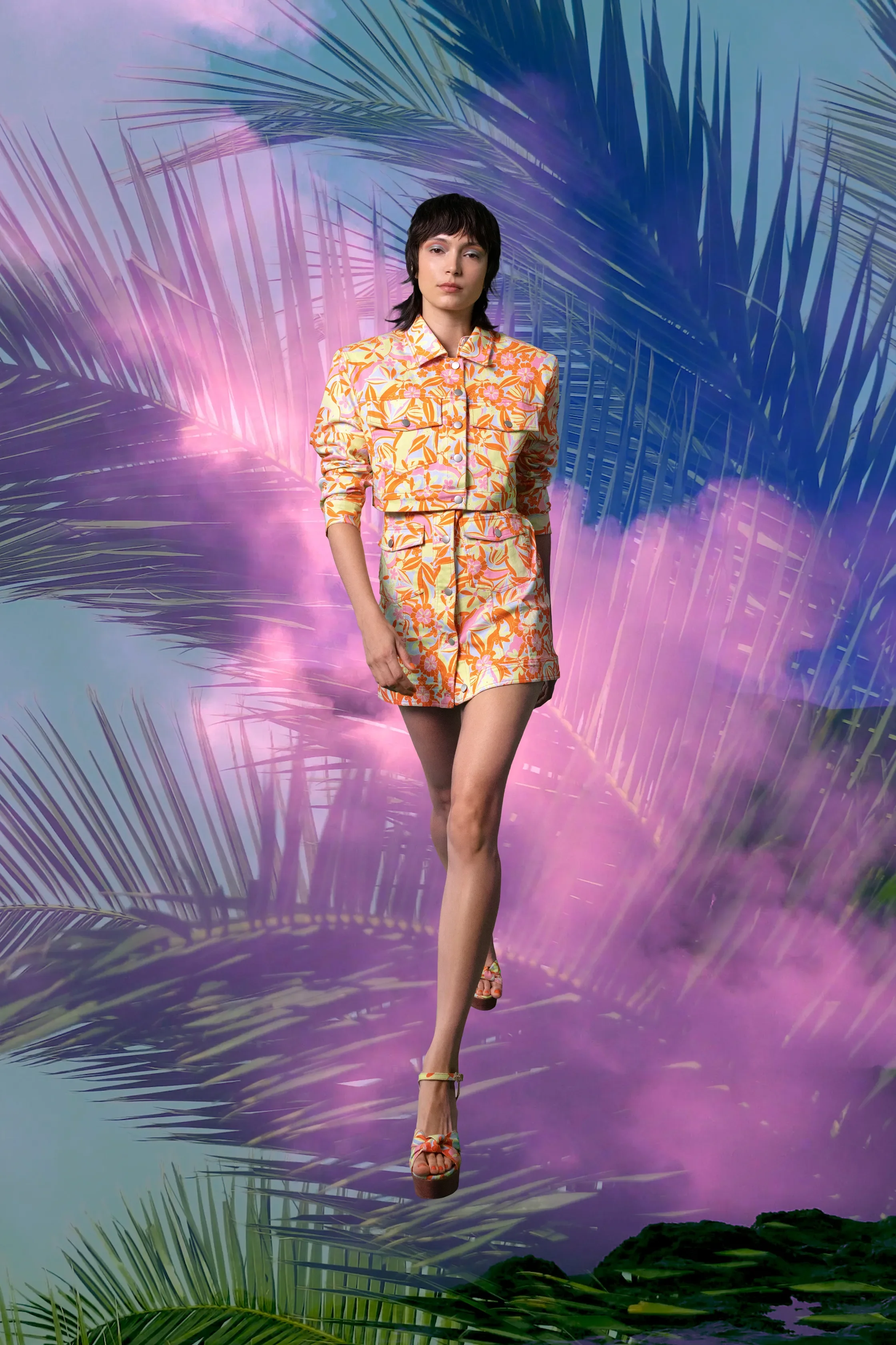 A woman walking on a pink reflective surface surrounded by tropical palm leaves with a colorful, vibrant background.