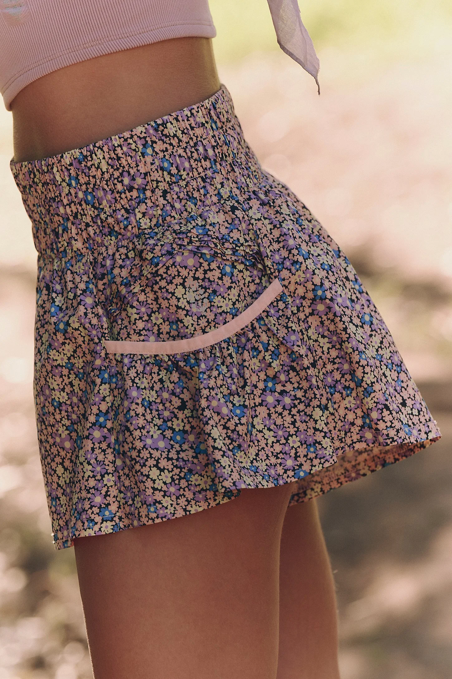 Close-up of a person wearing a pink crop top and a floral patterned skirt with a small pocket, outdoors with blurred background.
