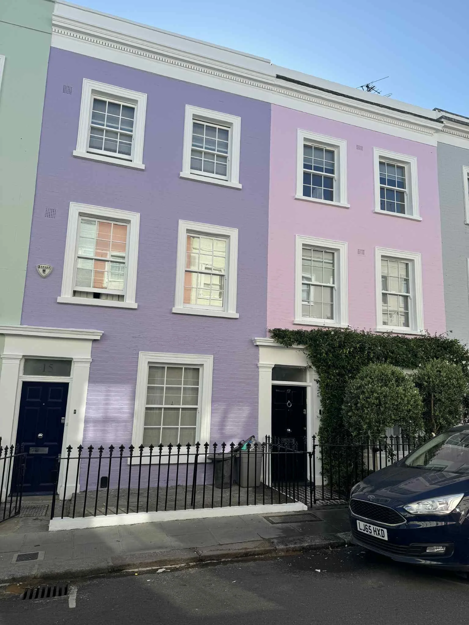 Colorful residential buildings with pastel purple, pink, and mint green facades, white window trims, and black gates in an urban street setting.