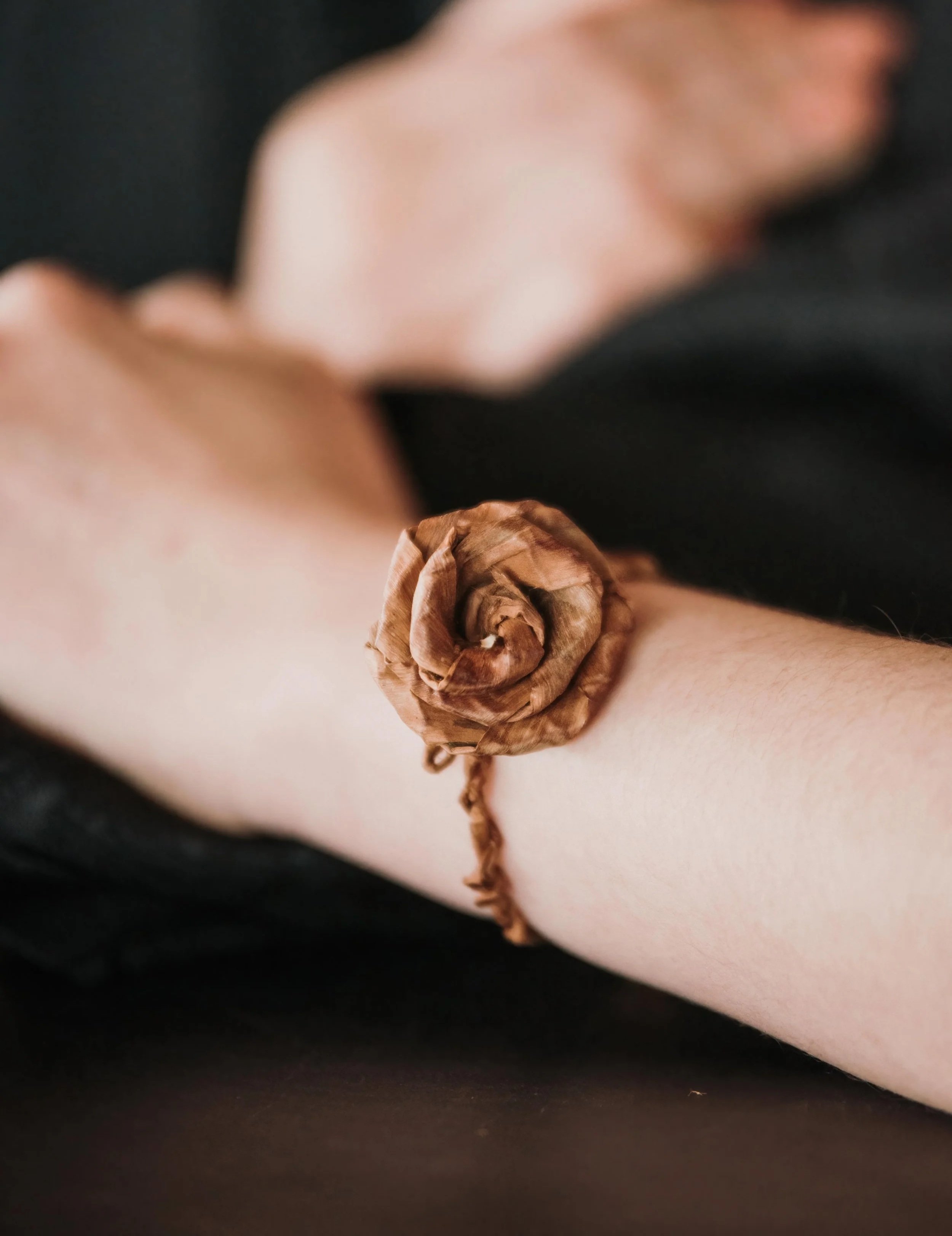 Close-up of a person's wrist with dried cedar rose accessory, wearing a black shirt.