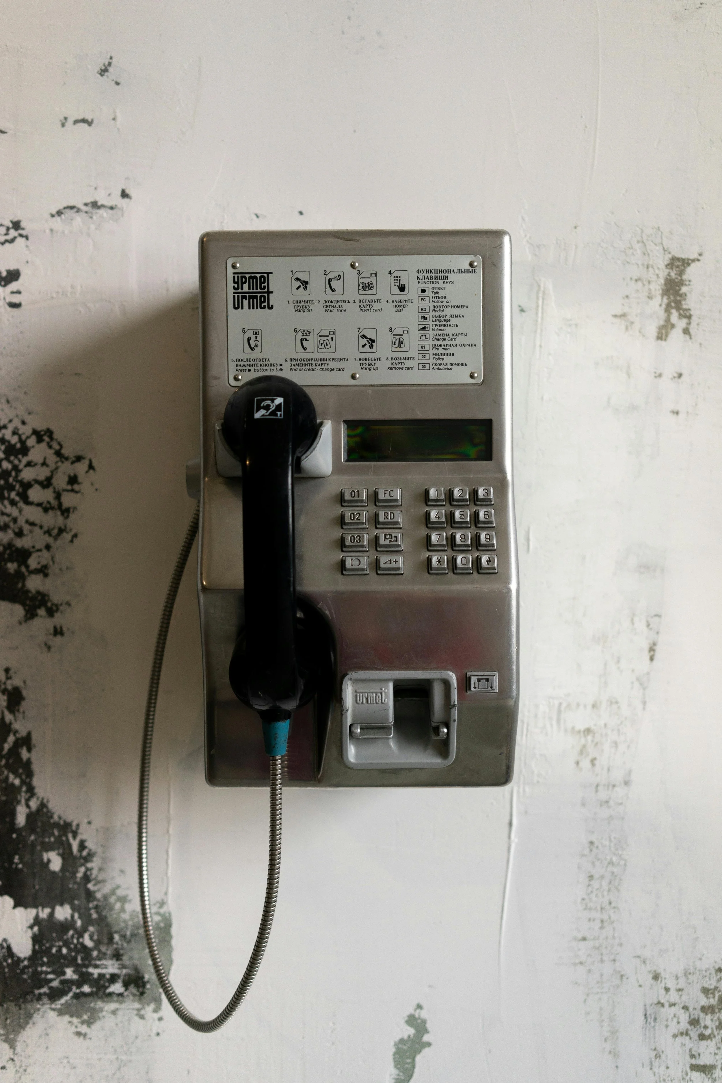 Mounted public telephone with keypad, display, and instructions on a textured wall.