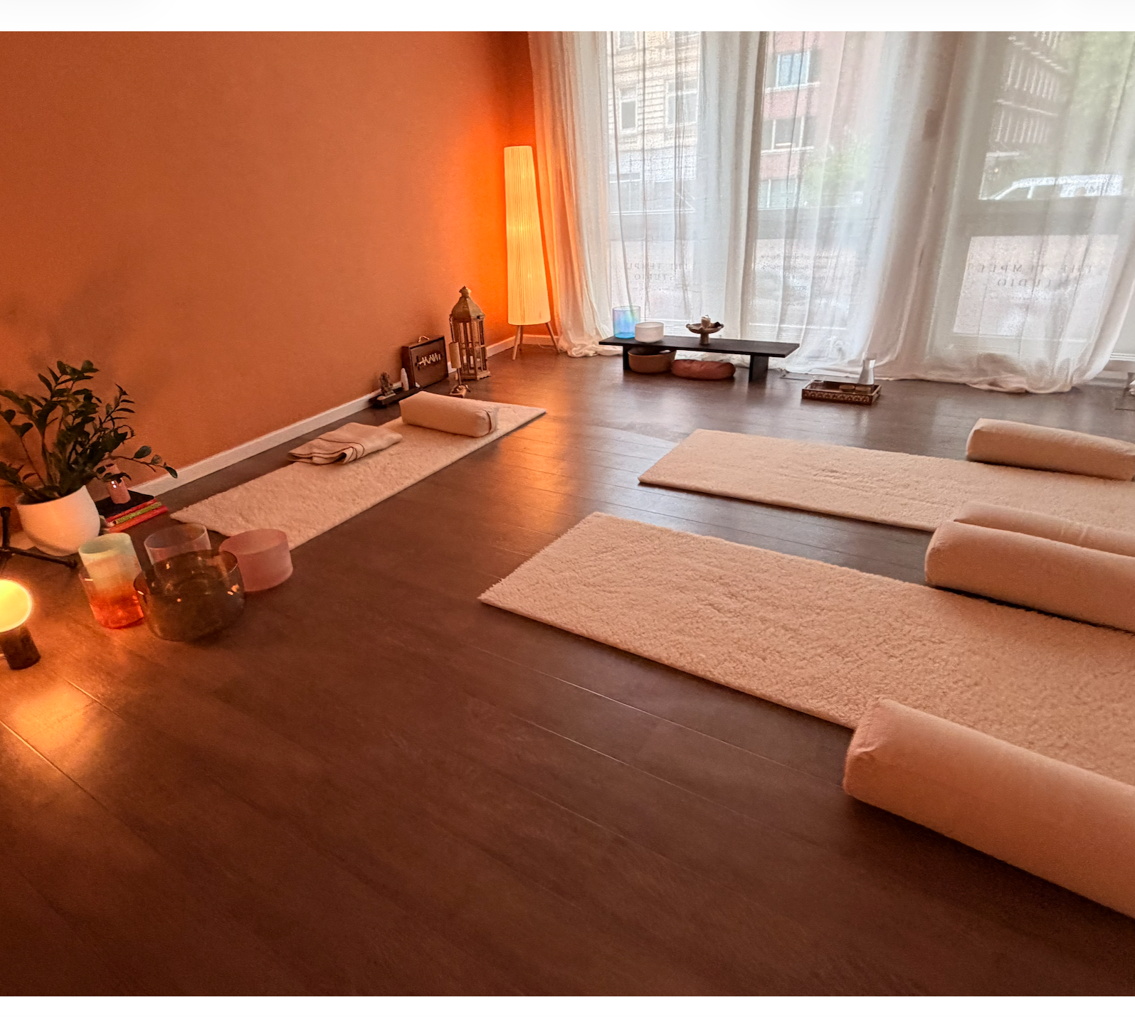 Gemütlicher Raum mit Yogamatten, Kerzen, Pflanzen und Dekoration im warmen Licht, große Fenster mit Vorhängen