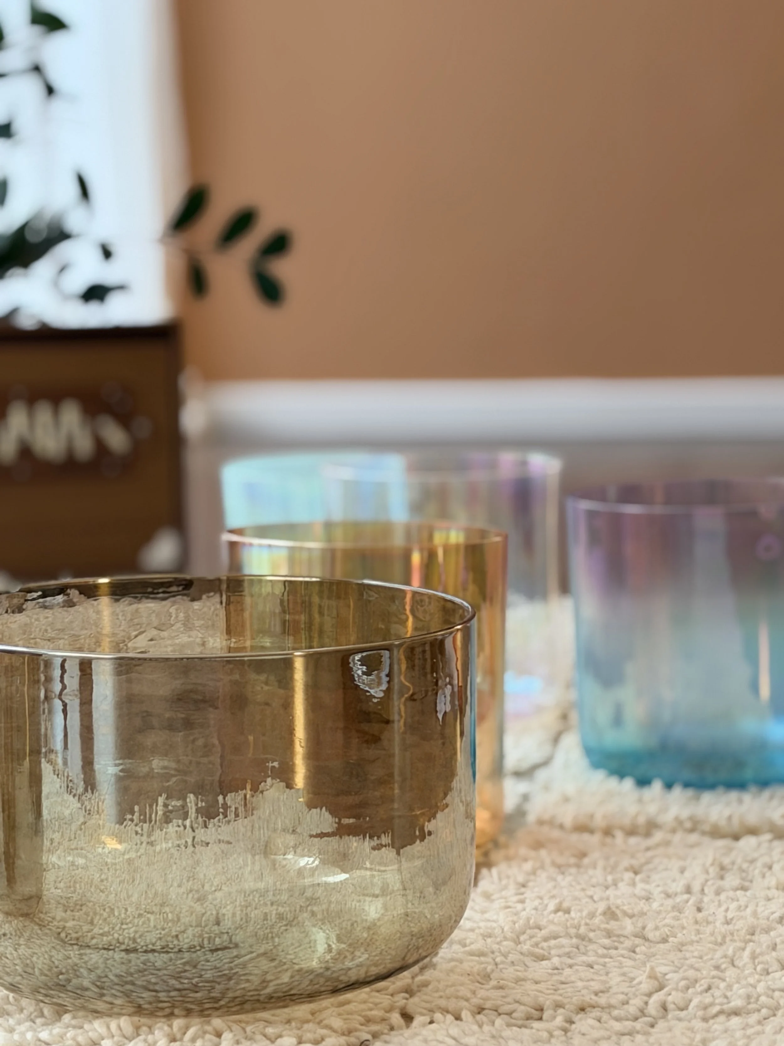 Set of four crystal bowls , iridescent, and blue colors displayed on a textured beige surface.