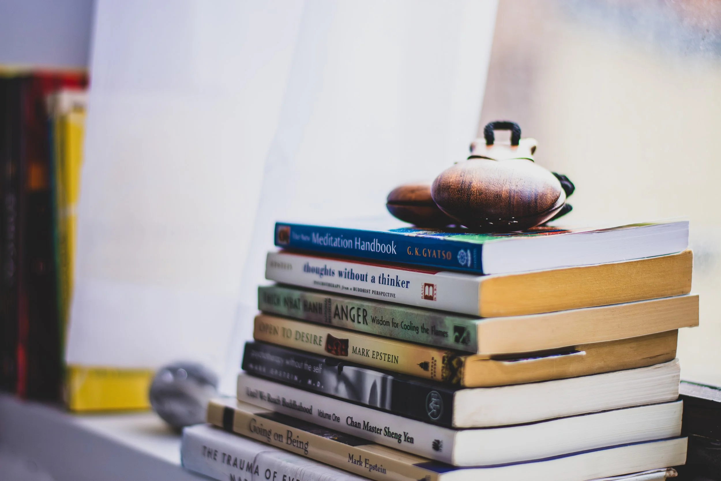 A stack of books on a white surface with a small wooden object on top of the books.