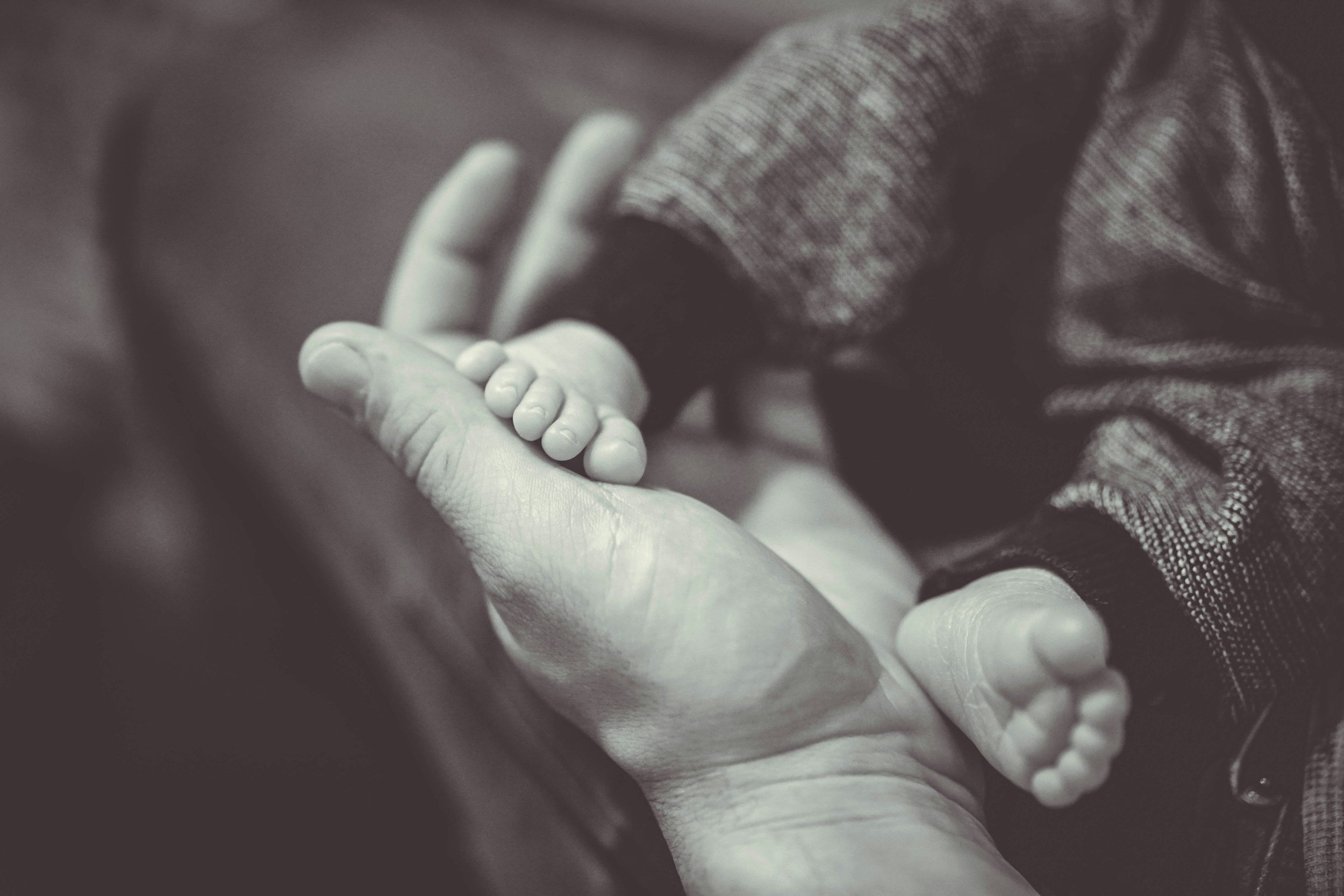 Adult hand gently holding newborn baby’s feet