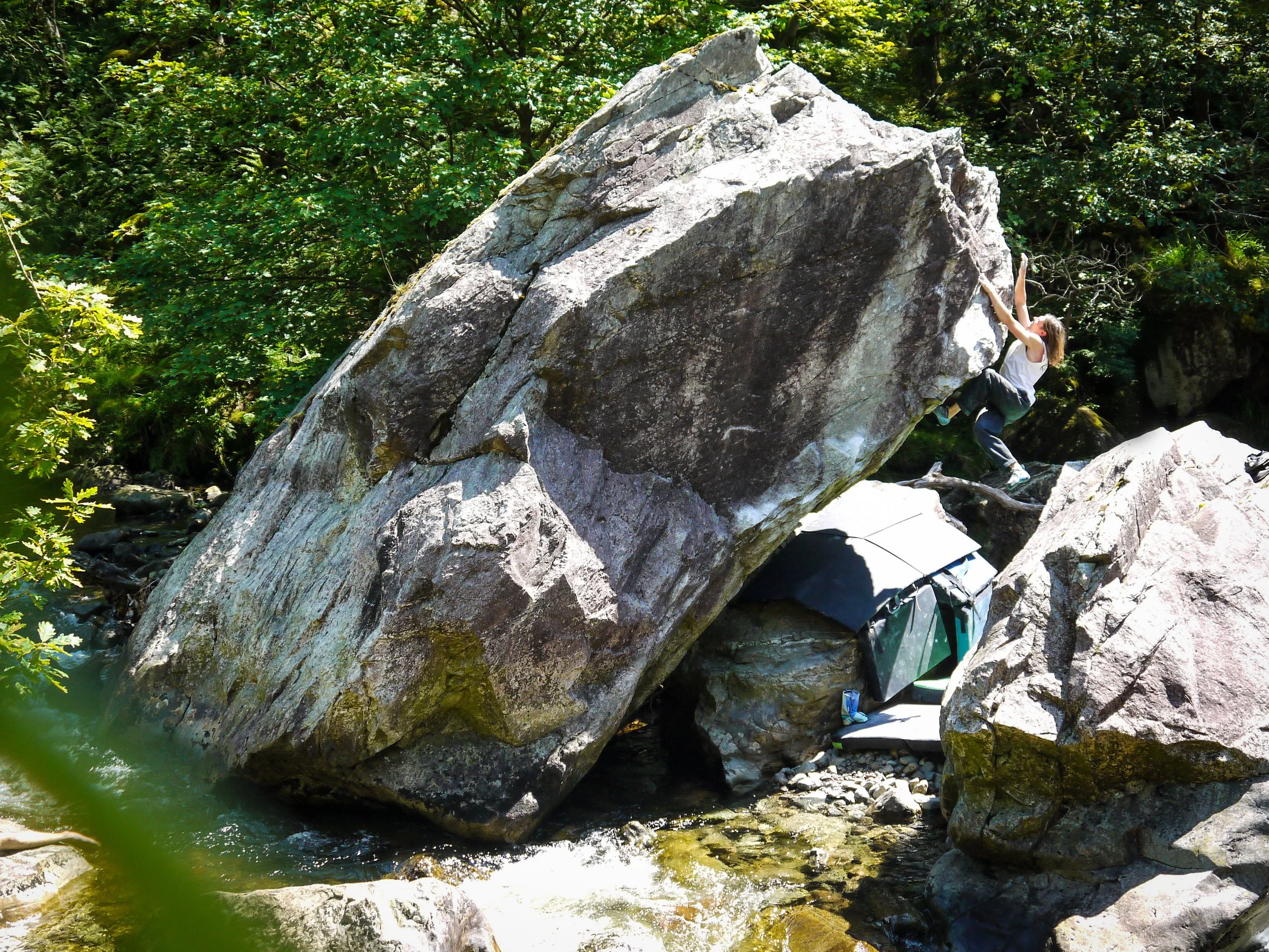 A woman cliff climbing on a large boulder near a stream in a forest.