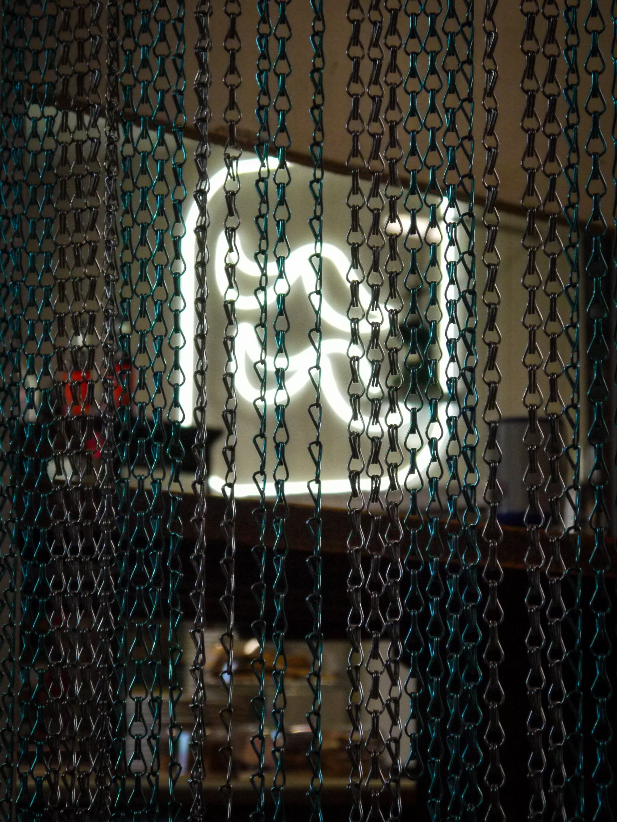 View of a sofa and floor lamp visible through a beaded curtain with metal chains, hanging in the foreground.