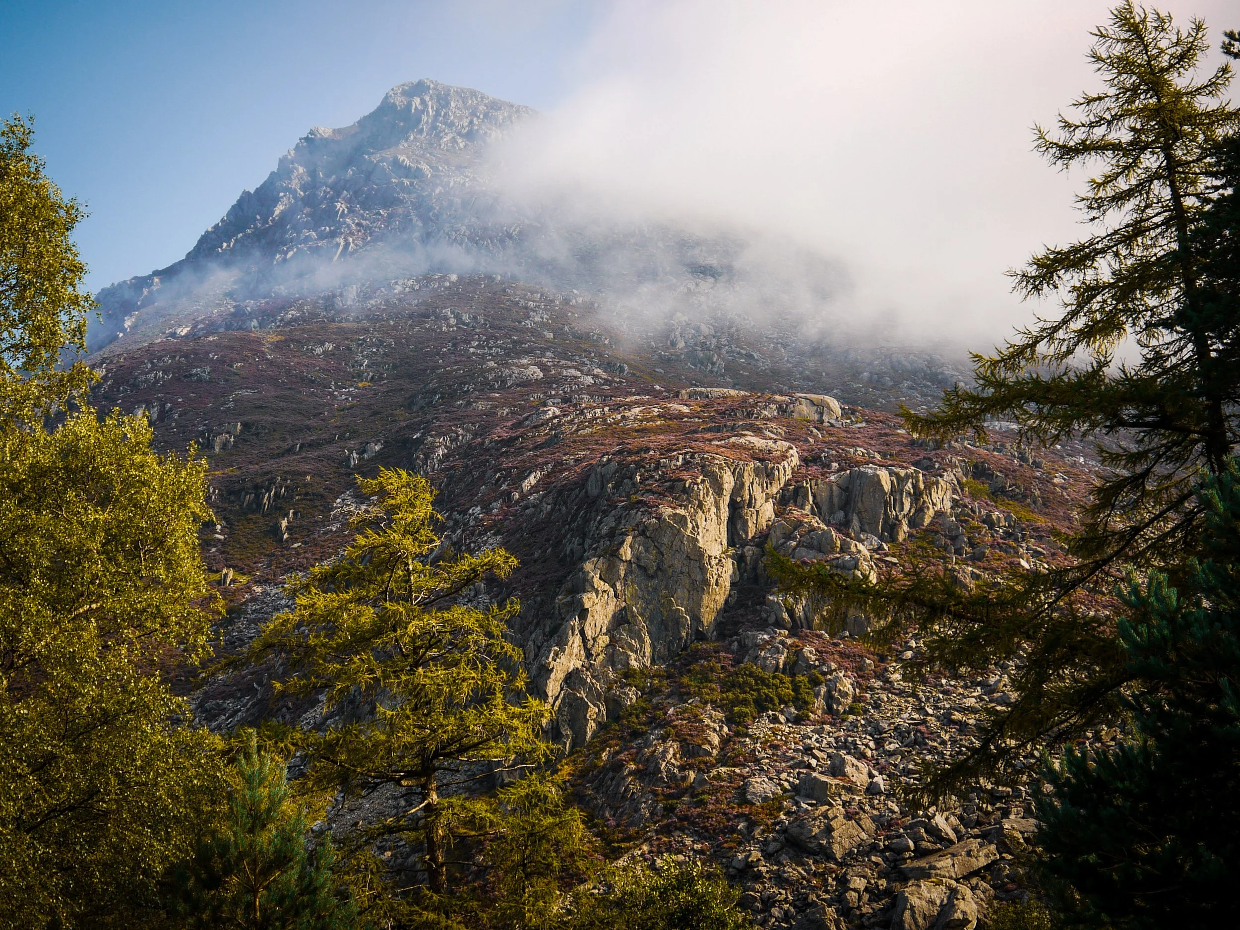Mountain landscape with rocky slopes, surrounded by trees, with mist or clouds near the mountain top.