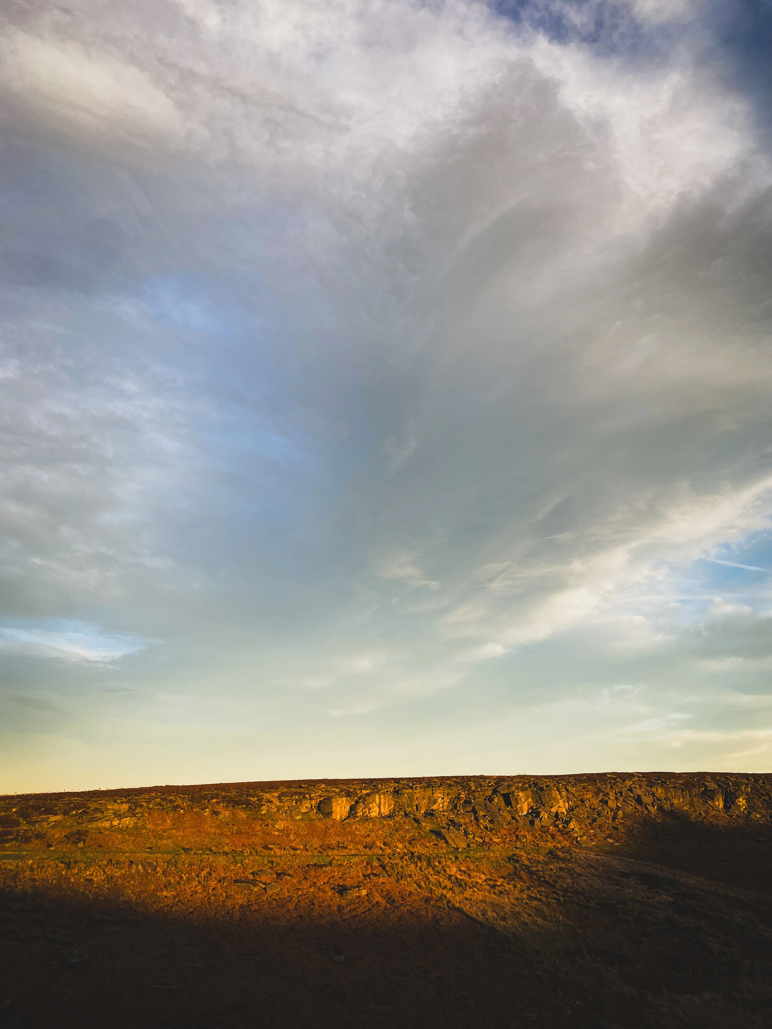 A landscape with a rocky hill under a partly cloudy sky at sunset.