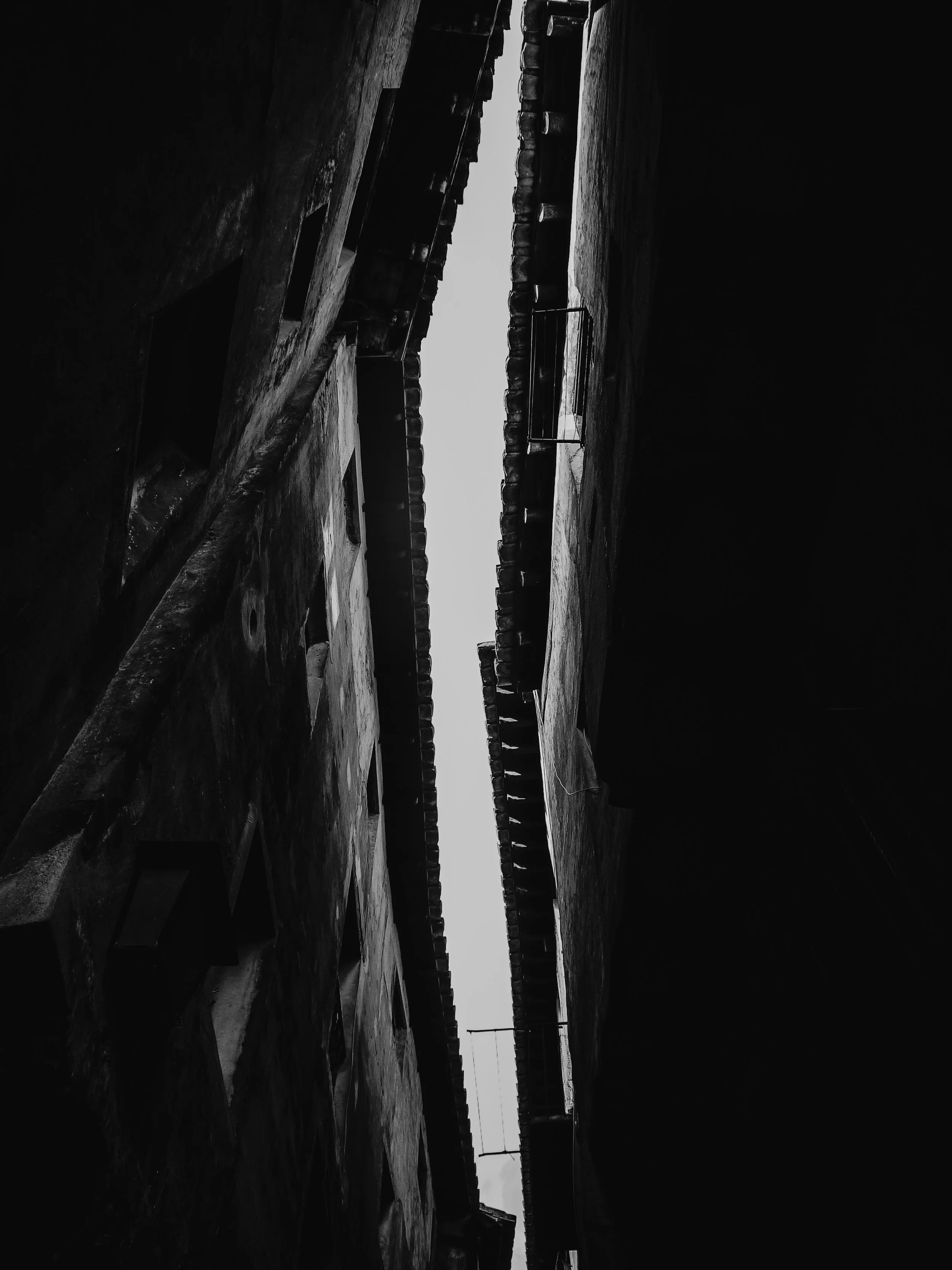 Black and white photo of the narrow alleyway between two old buildings, with clothes hanging on a line across the gap.