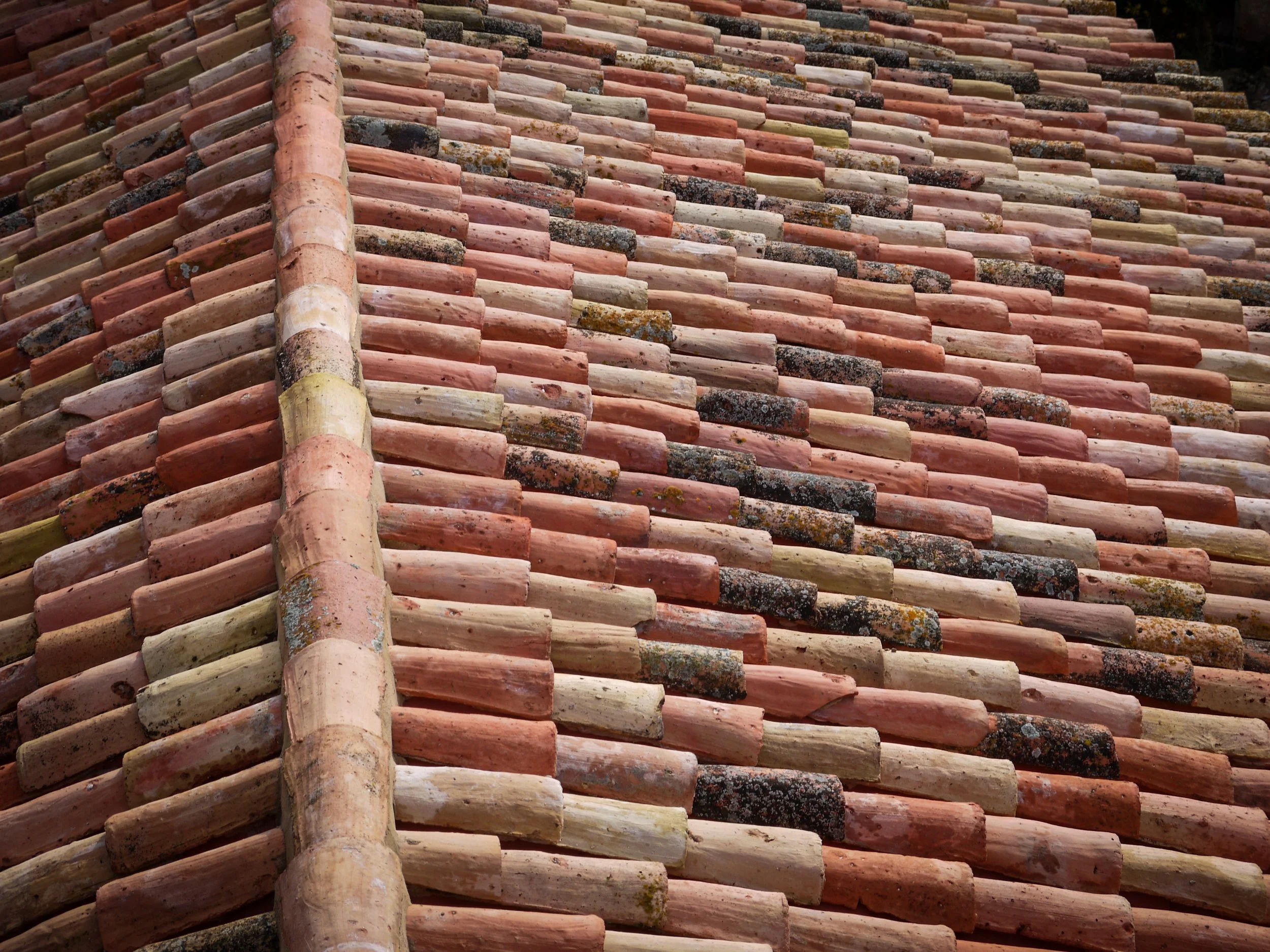 Close-up of a roof made of red, pink, and black weathered clay tiles arranged in overlapping rows.