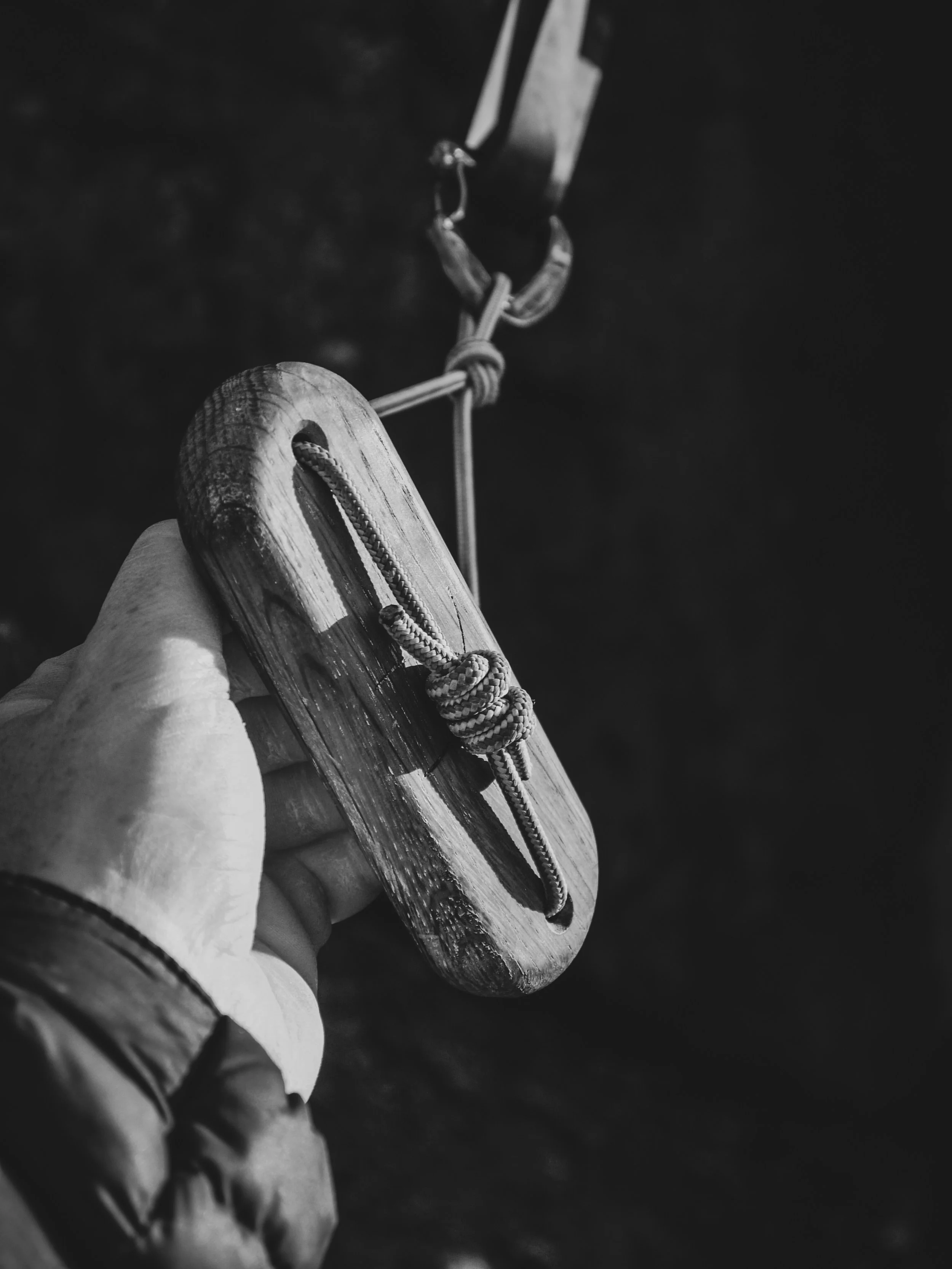 A person holding a wooden climbing tool with a coil of rope, attached to a climbing harness or anchor point.